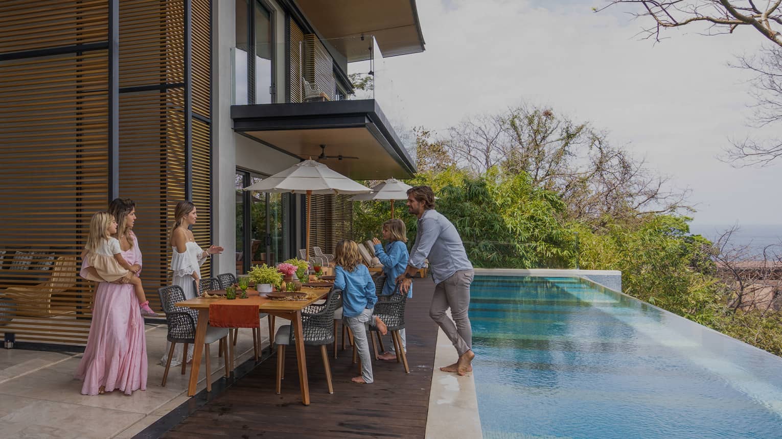Family gathers around dining table set outside on a deck next to a private infinity-edge pool