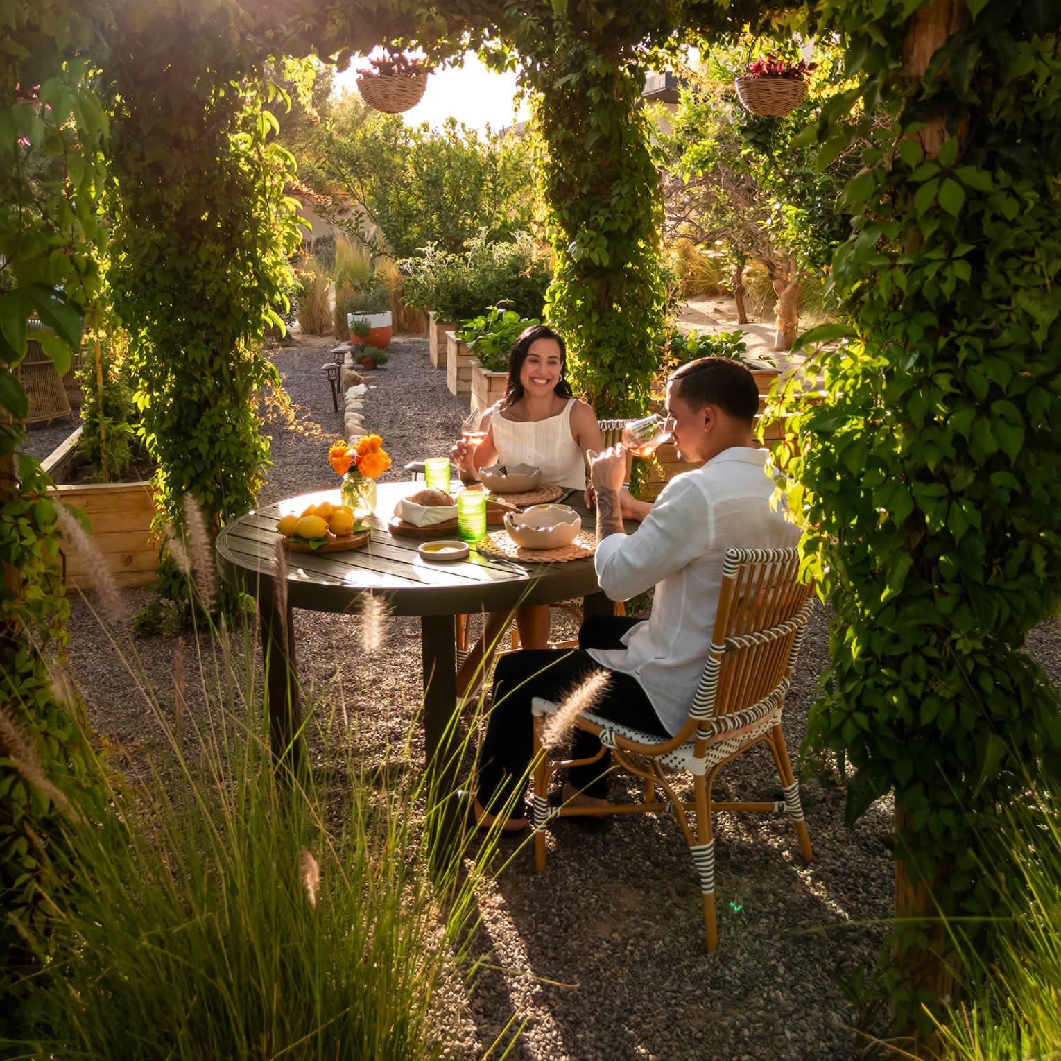 Two people at a small outdoor dining table in an outdoor space surrounded by lush greenery