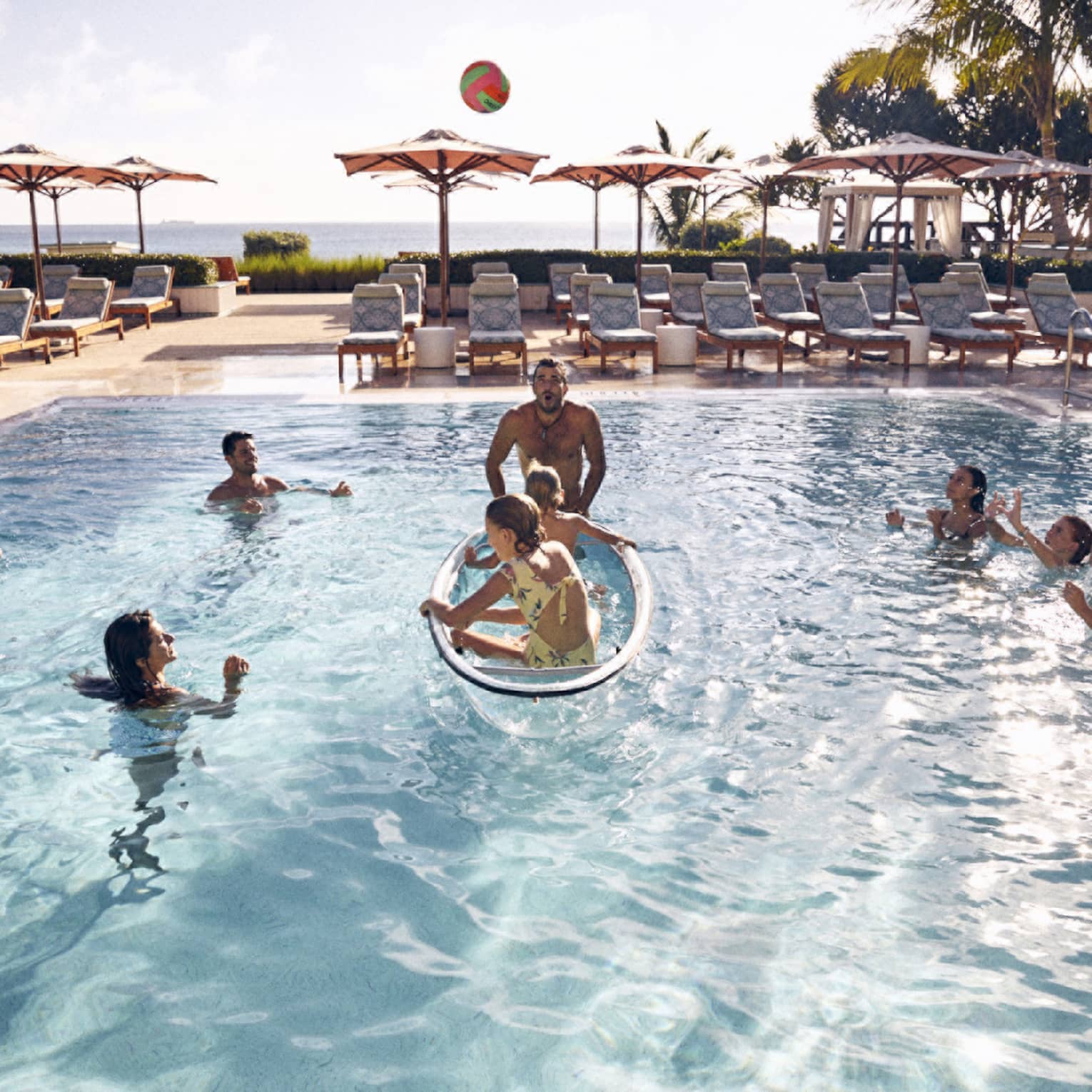 Guests in the pool with palm trees and the ocean in the background.