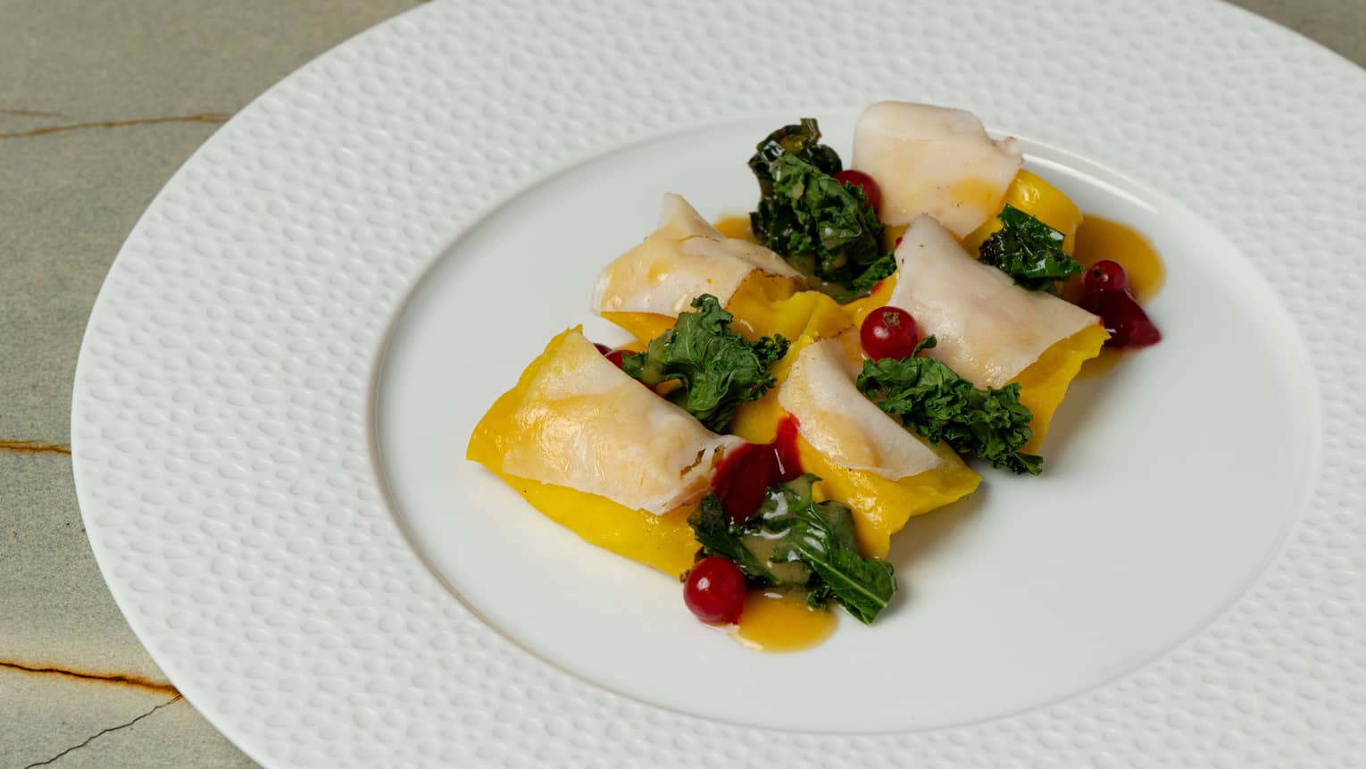 A round white plate with a wide textured edge holds food items topped with green and red garnishes.
