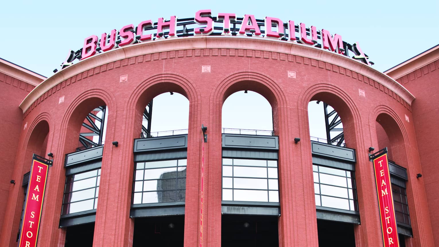 Red neon Busch Stadium sign over curved brick building, green awnings