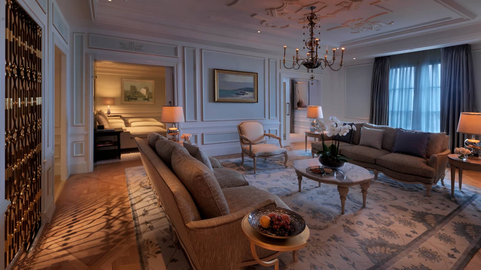 Large, dimly-lit Khazar Presidential Suite living room, area rug, antique-style chandelier