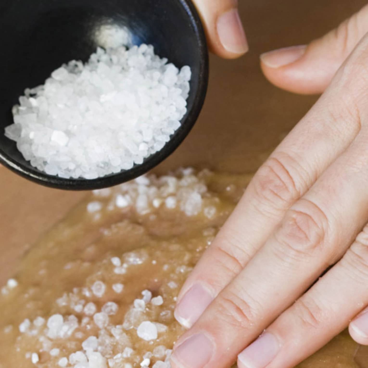 Close-up of large spa salts in bowl, hand rubbing crystals on bare back