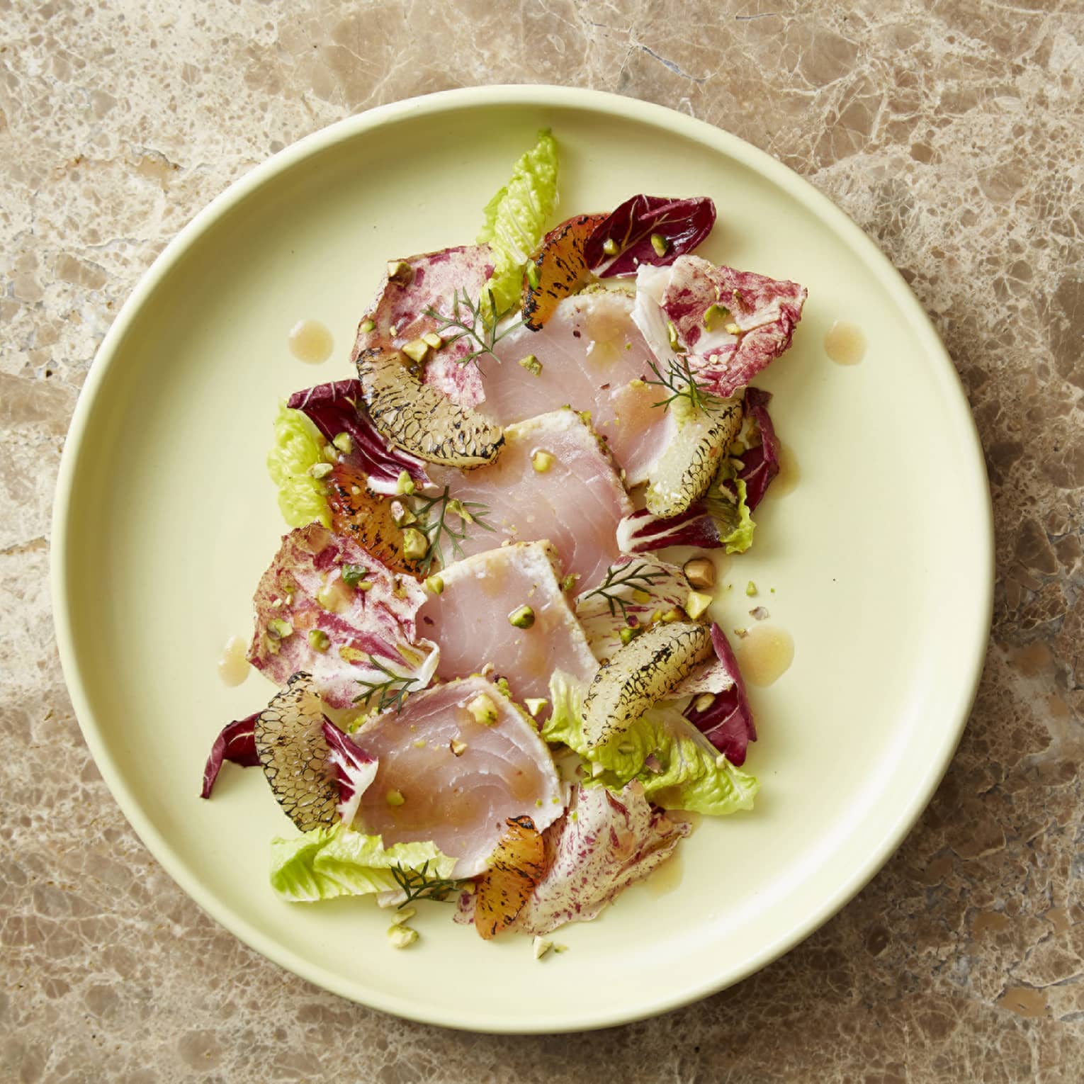 Swordfish, citrus, pistachio and radicchio on a light yellow plate