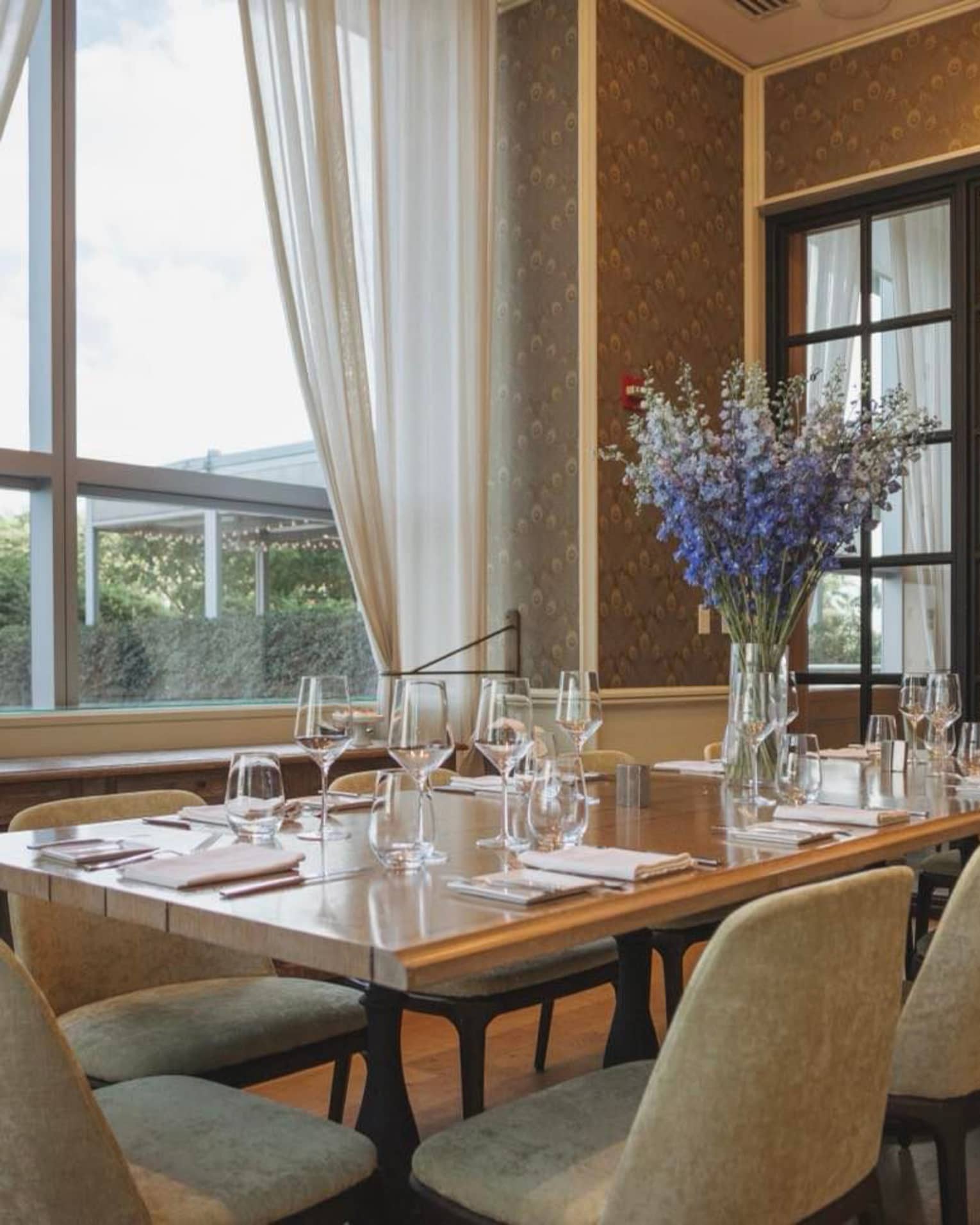 A large dining table with blue flowers near a large window.