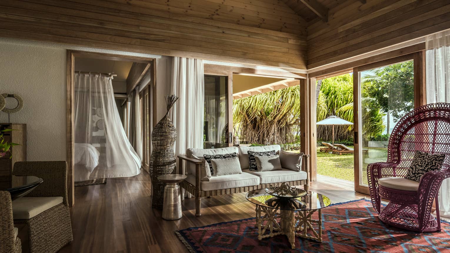 One-bedroom suite living room wicker furniture under wood beam roof, bed with white sheer canopy