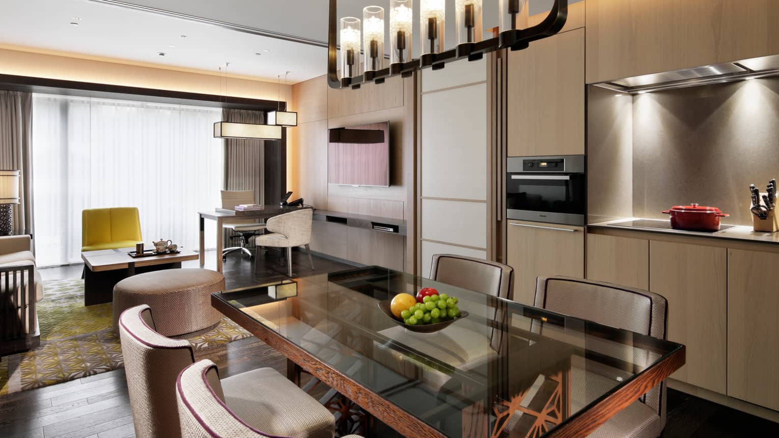 Modern open-plan living and dining area with a glass dining table, kitchenette and cozy seating area