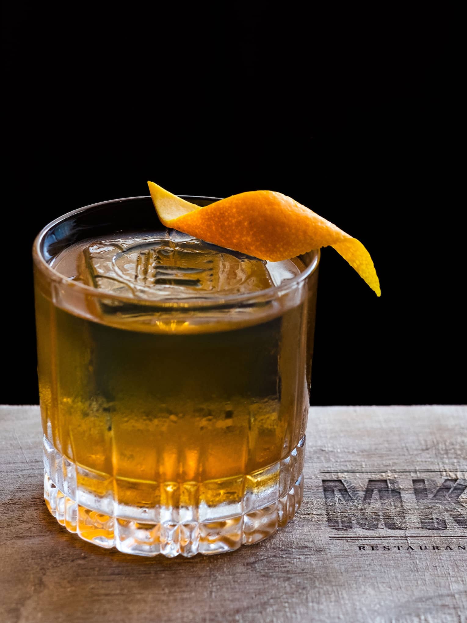 A close up of an Old Fashioned cocktail garnished with an orange peel swirl