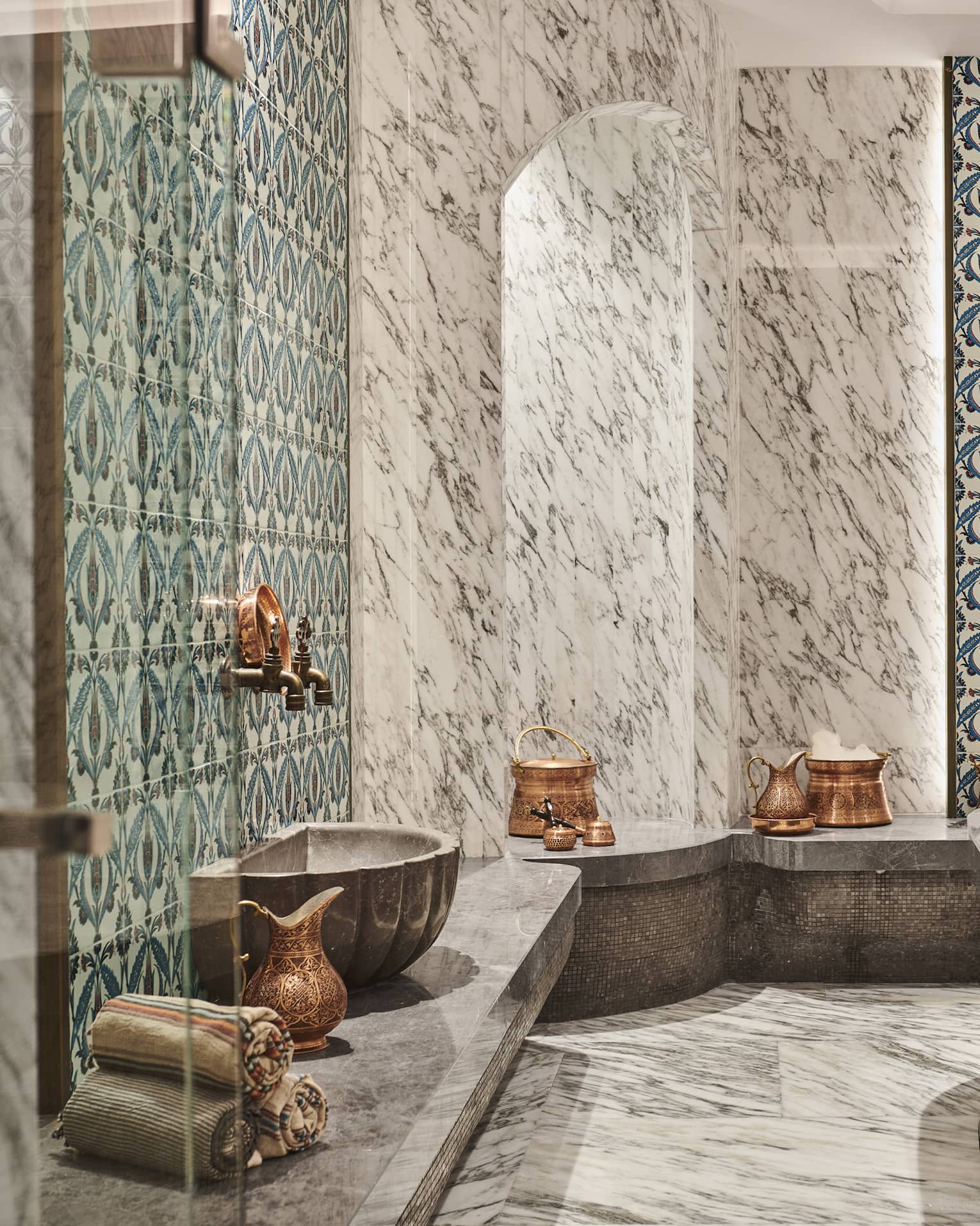 Steam shower with mosaic tile and full marble walls, floor and benches, and brass urns