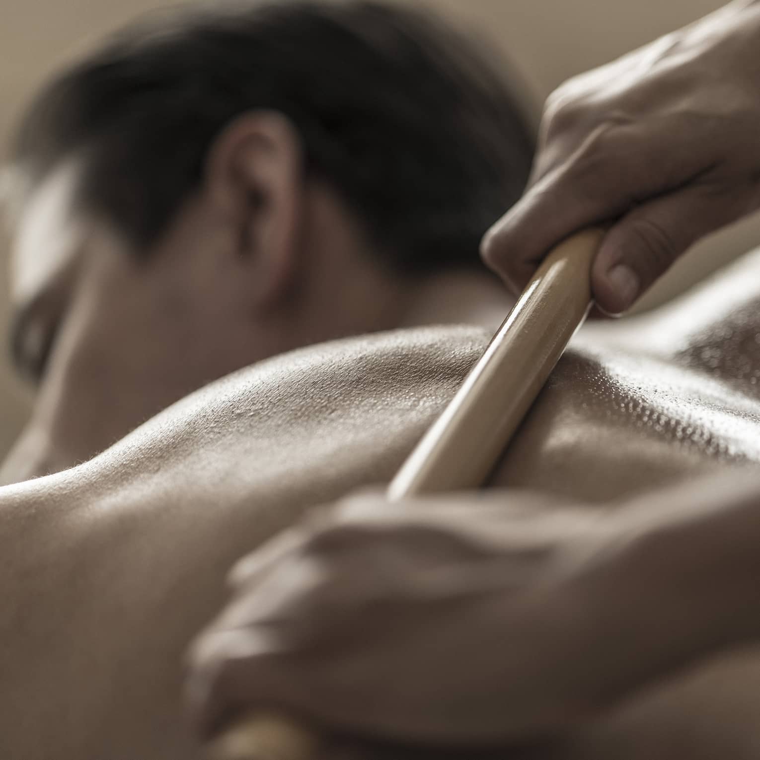 A spa attendant uses a tool to massage a guest's back