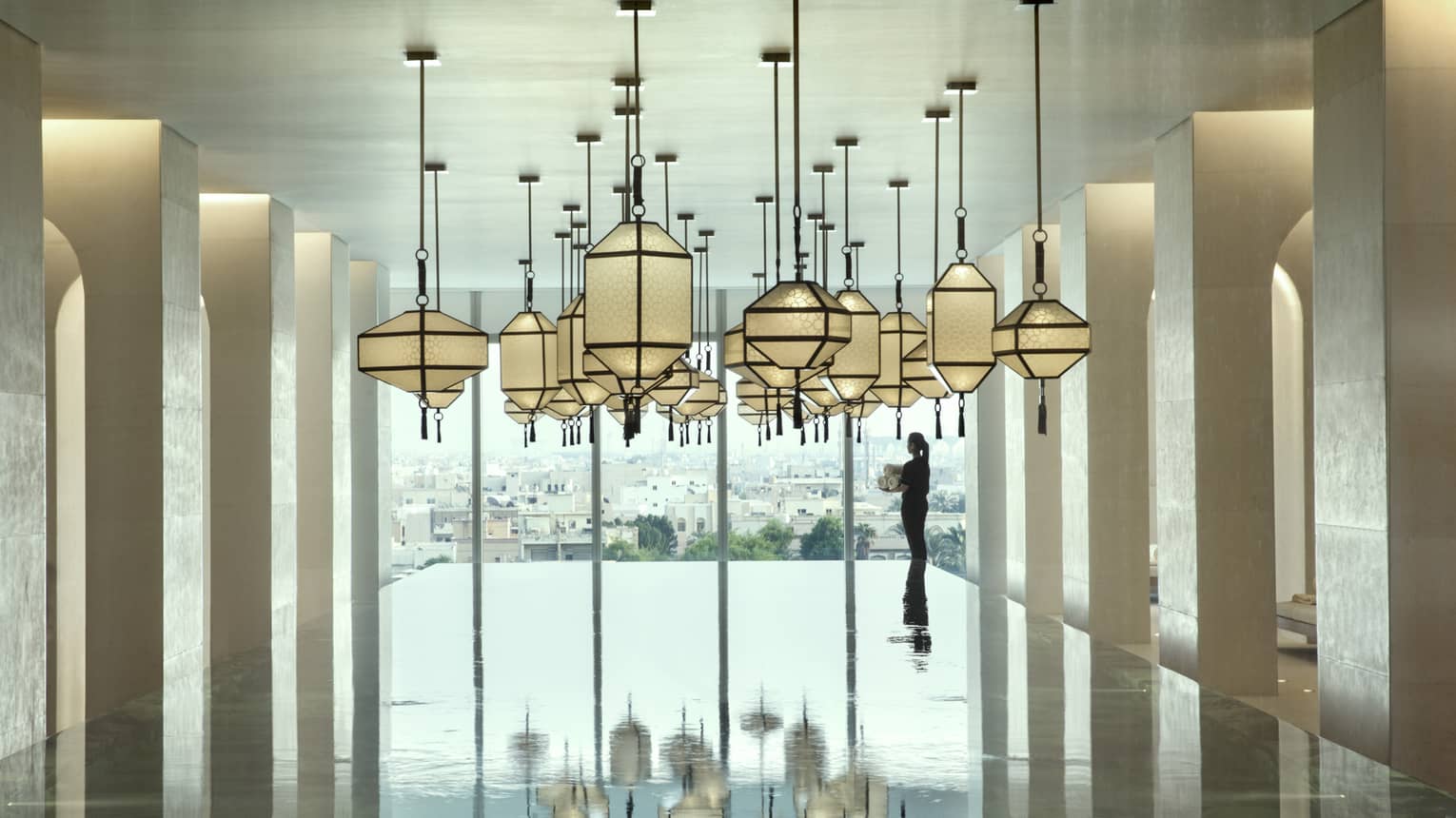 A Four Seasons member walks around the indoor pool that overlooks the city and has glass lanterns hanging overhead