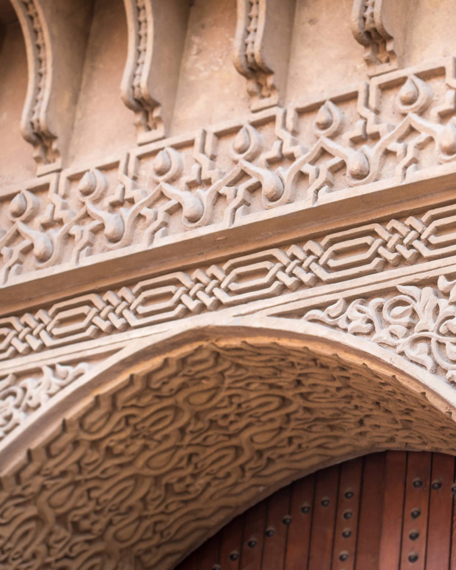 Extreme close-up of a stone entry with ornate carvings in floral and geometric patterns framing the top of a wooden door.