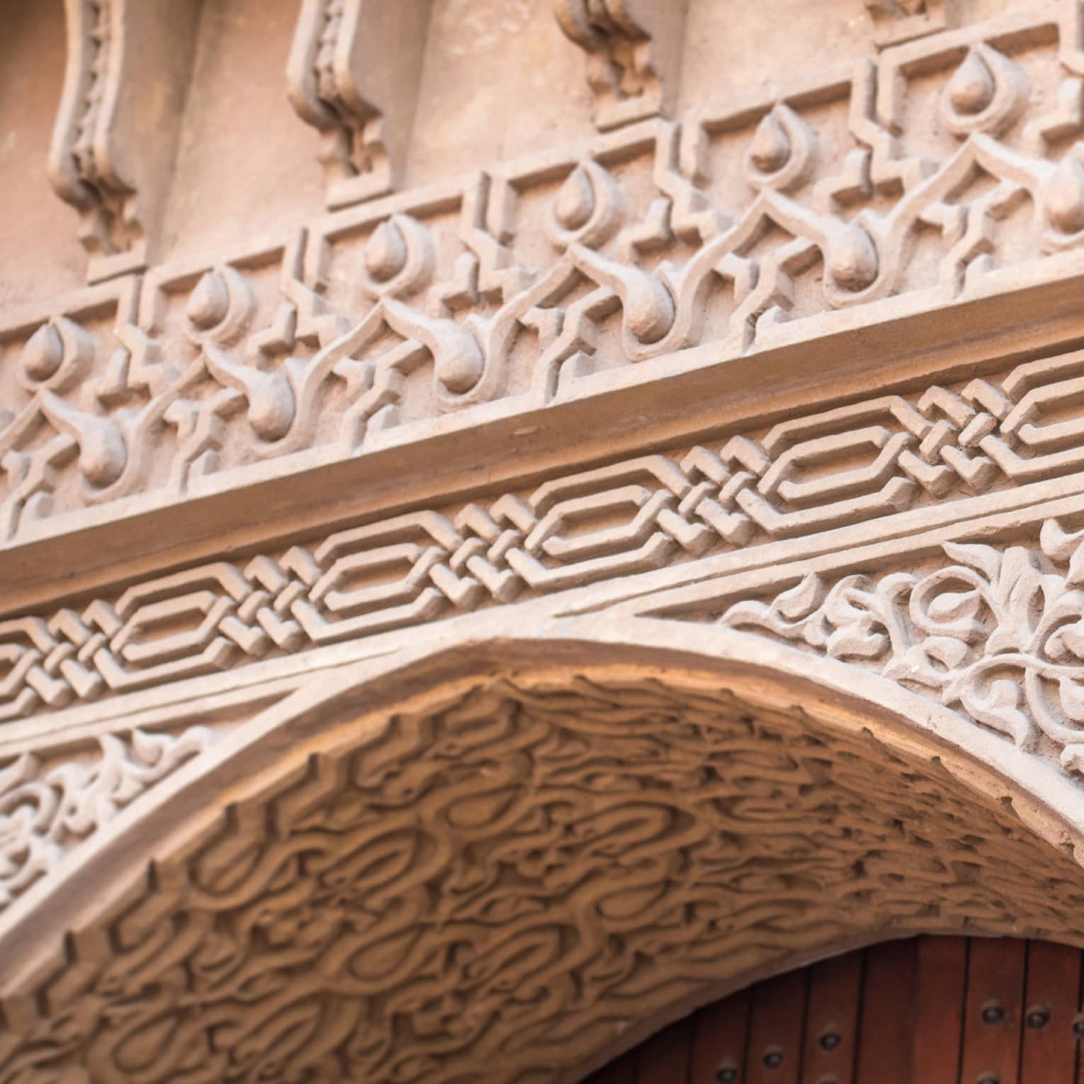 Extreme close-up of a stone entry with ornate carvings in floral and geometric patterns framing the top of a wooden door.