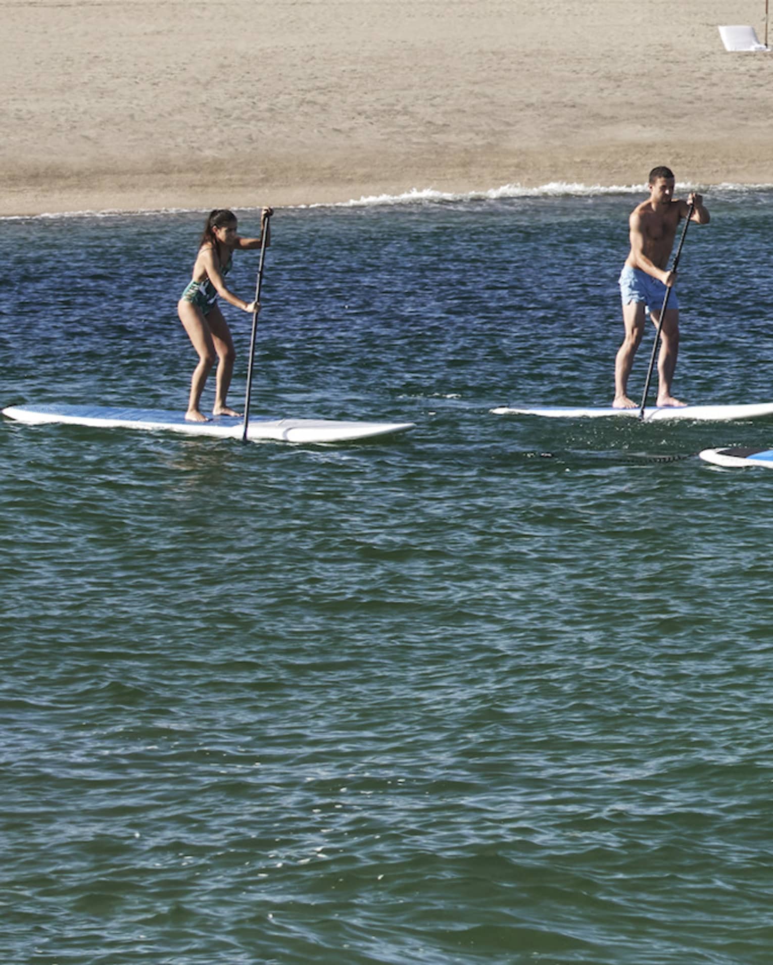 Three people on paddle boards in the water with a hotel behind them.