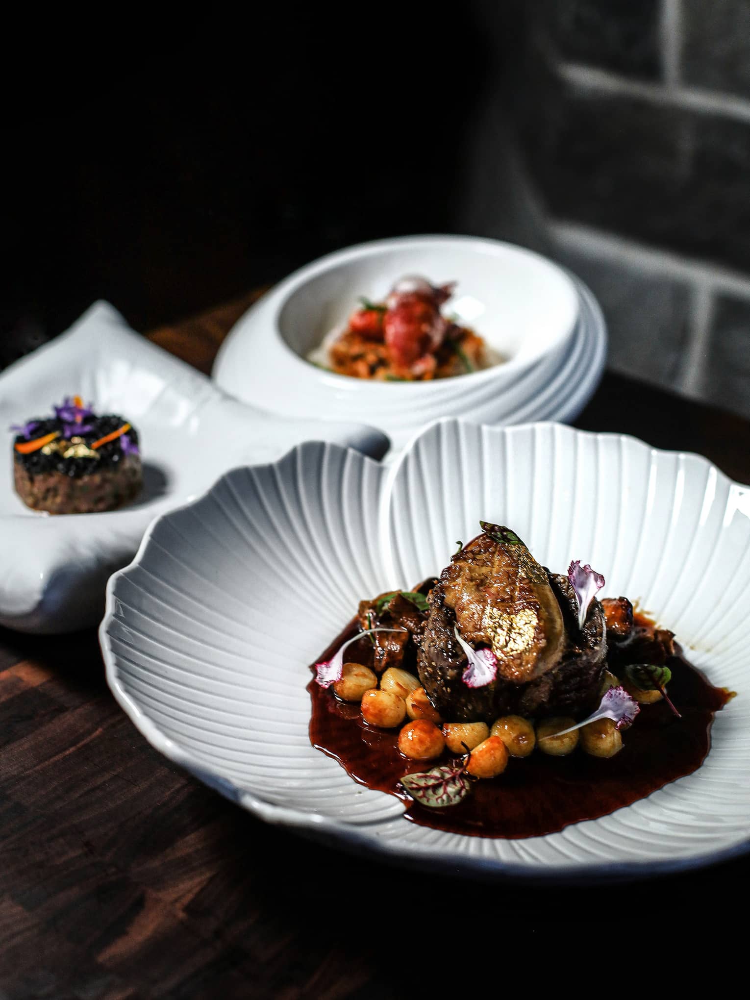 Three white plates of food set on a dark table with a dark backdrop