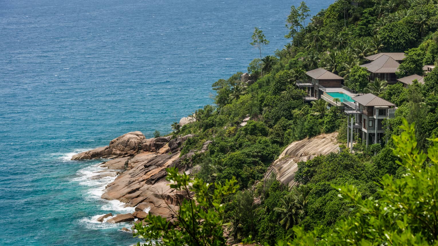 Aerial view of villas, swimming pool perched on mountain over cliffs, tropical forest, ocean below