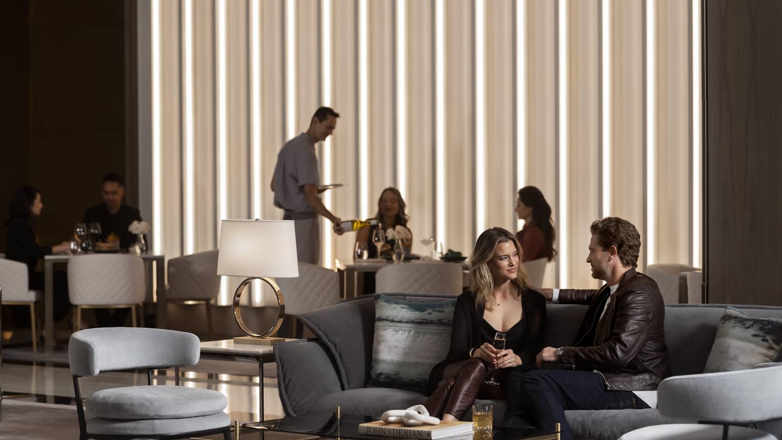 A man and woman sitting on a sofa with a group of people behind them near a large window.