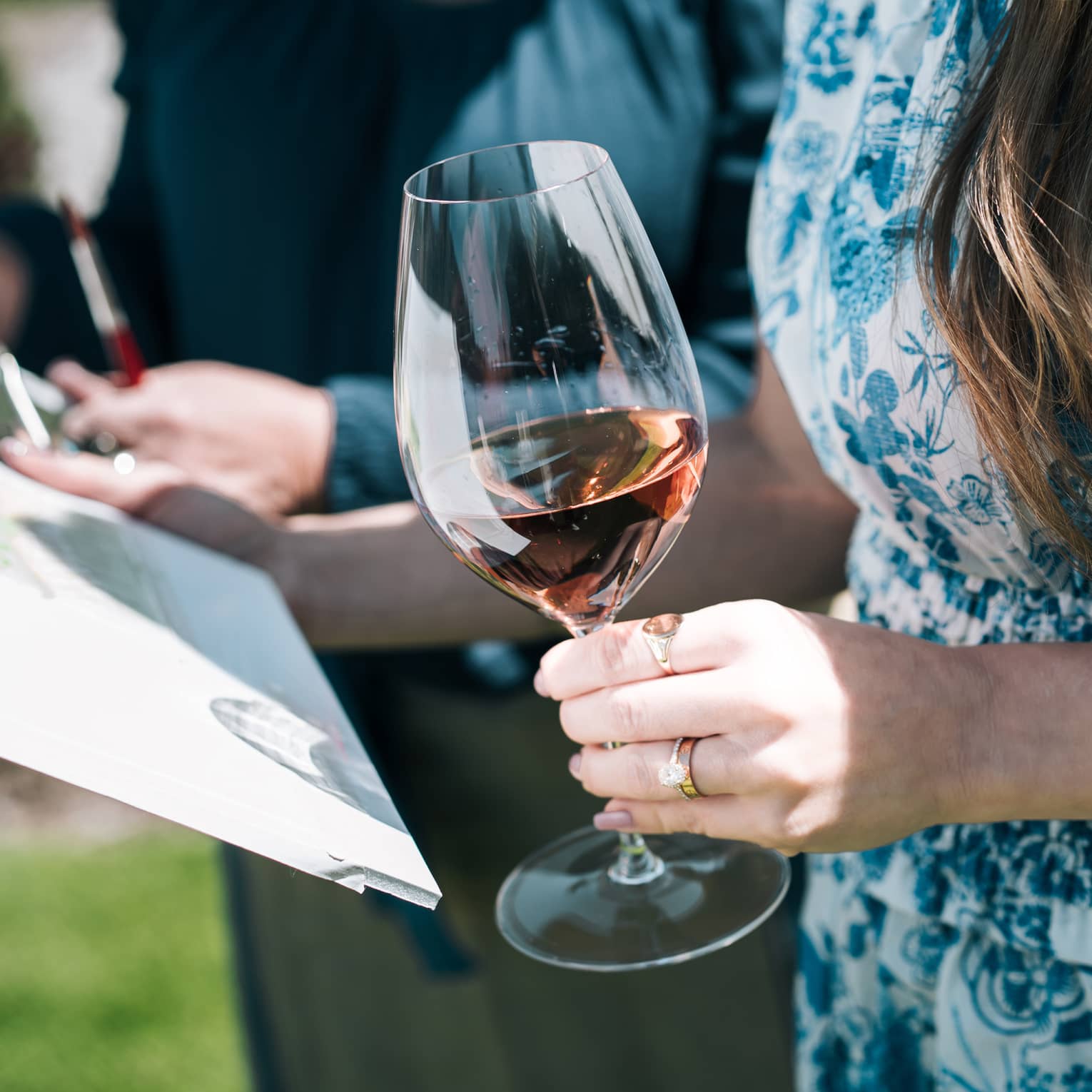Person holds a glass of wine in one hand while holding a painting in the other