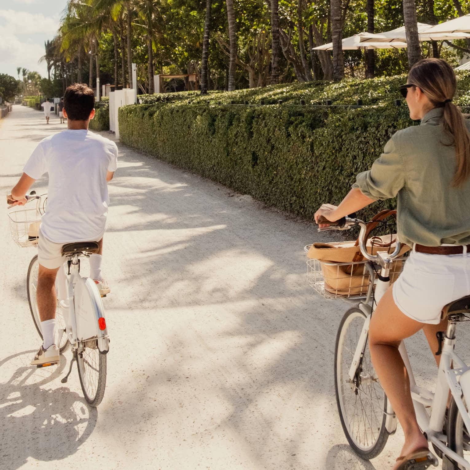 Two guests riding a bike on a sidewalk with green bushes on the side.