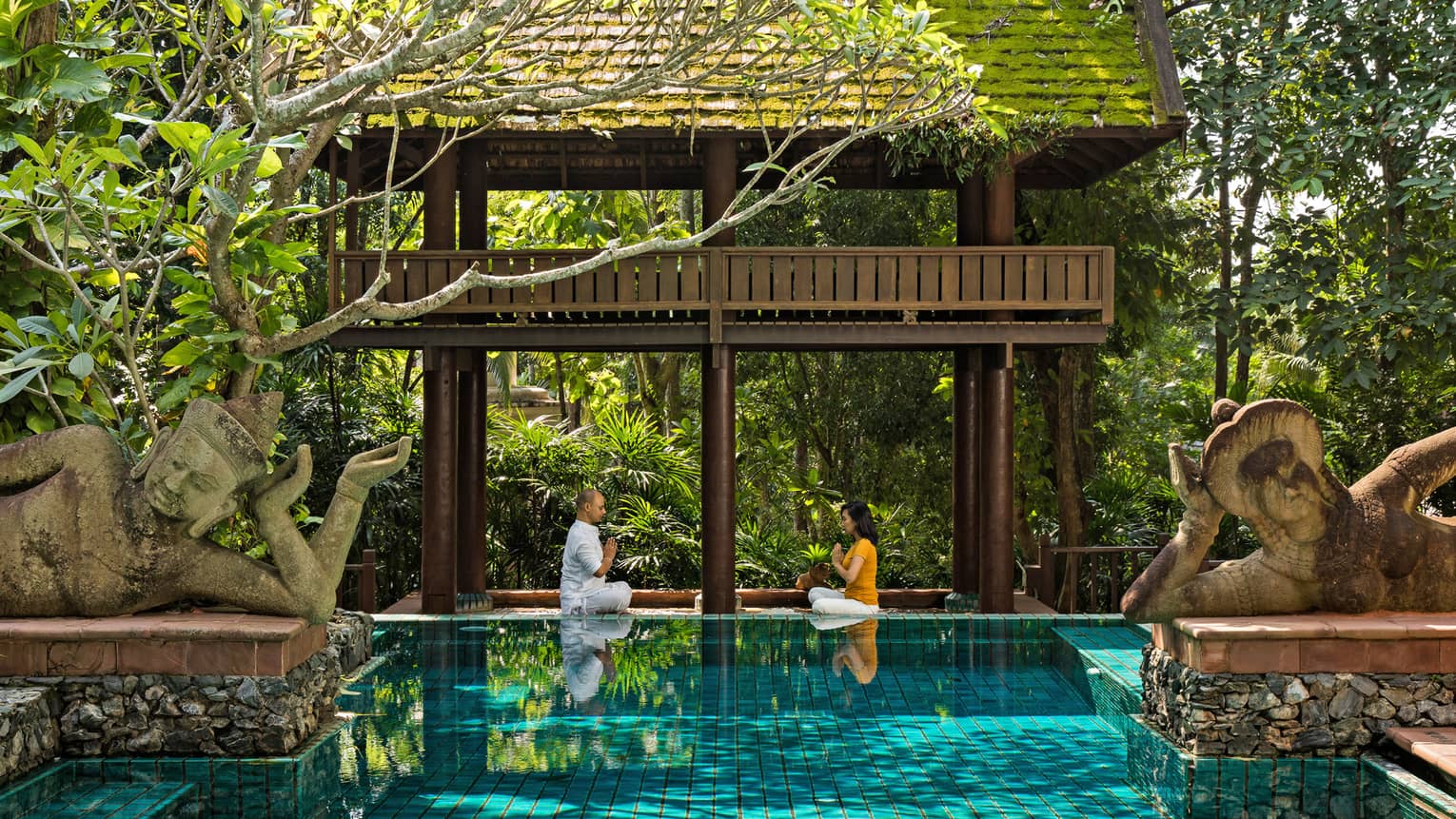 Couple practicing meditation in an outdoor pool setting 
