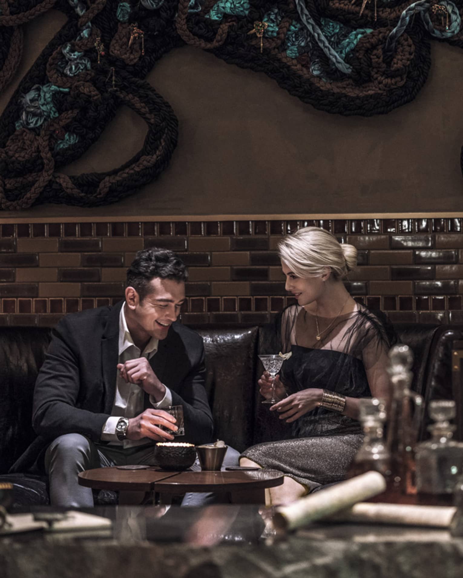 Man, woman drink cocktails on dark leather lounge sofa in Charles H lounge