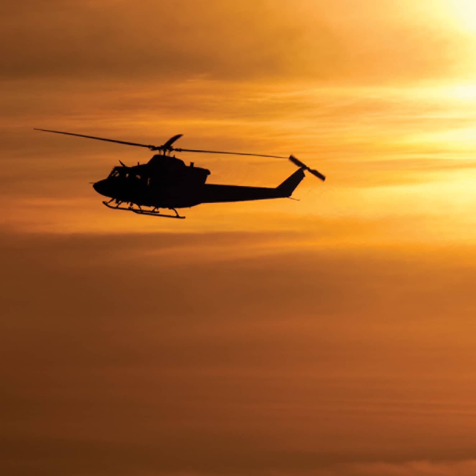 Silhouette of helicopter against orange sky