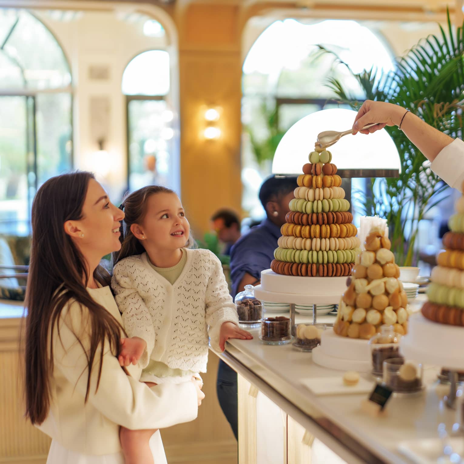 Parent holds a young child in her arms next to a display of macarons
