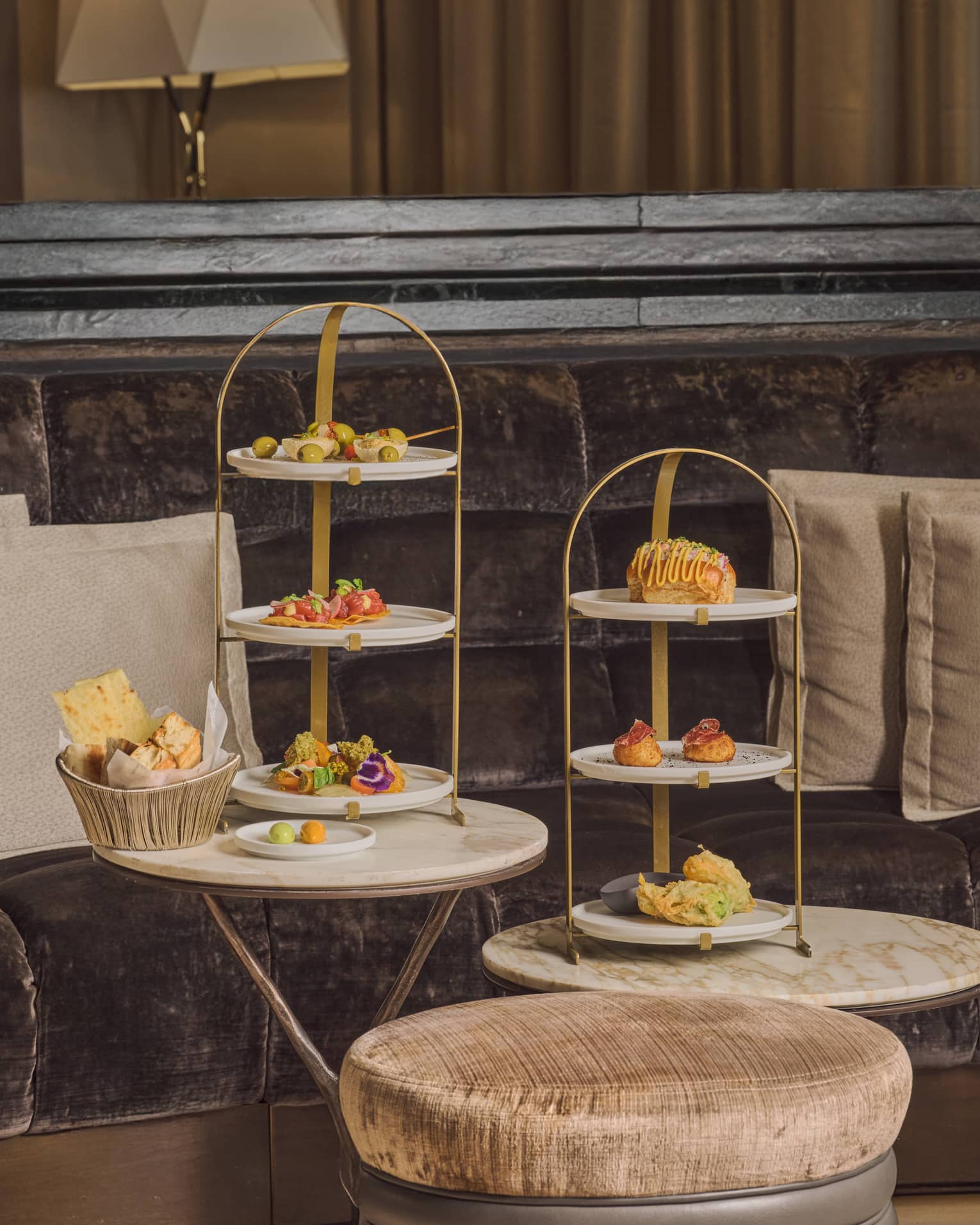 Three-tiered serving stands hold small bites and sit on small round tables in a restaurant setting.