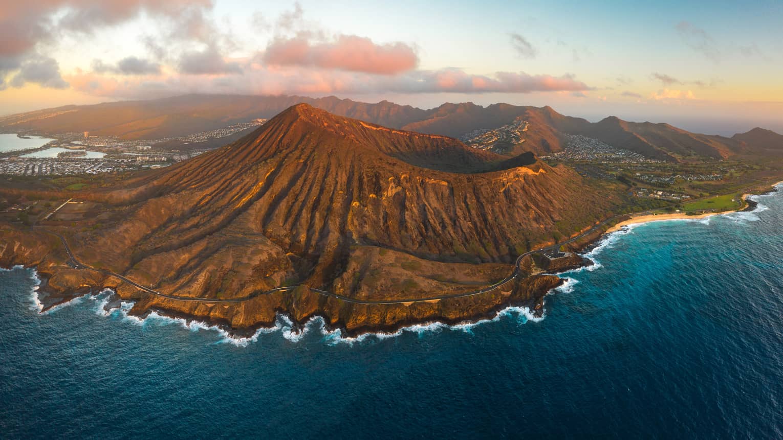 Aerial view of Koko Crater on Oahu with pink clouds in the background and dark-blue ocean in the foreground