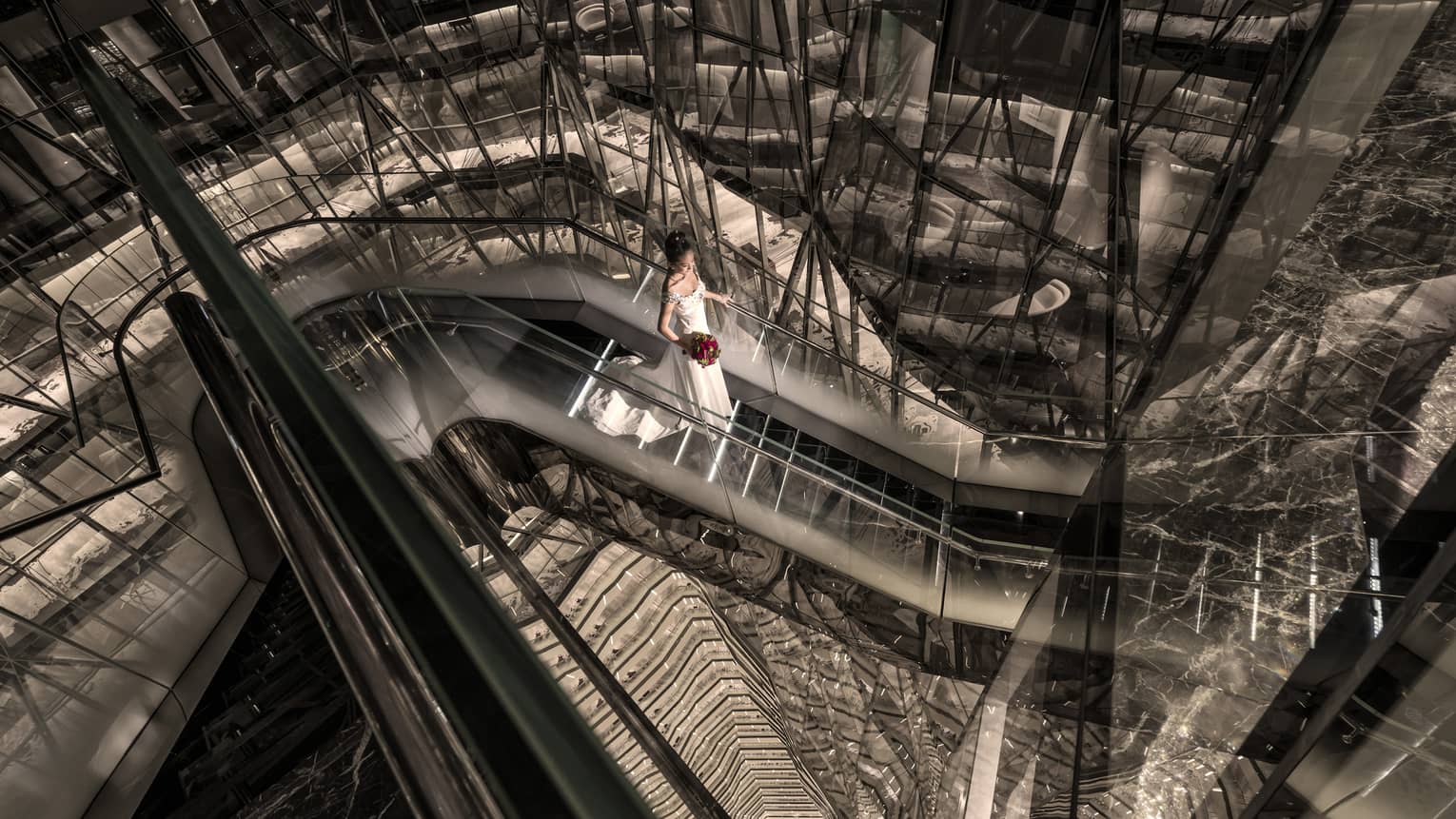 Bride wearing white gown walks down modern black and glass staircase
