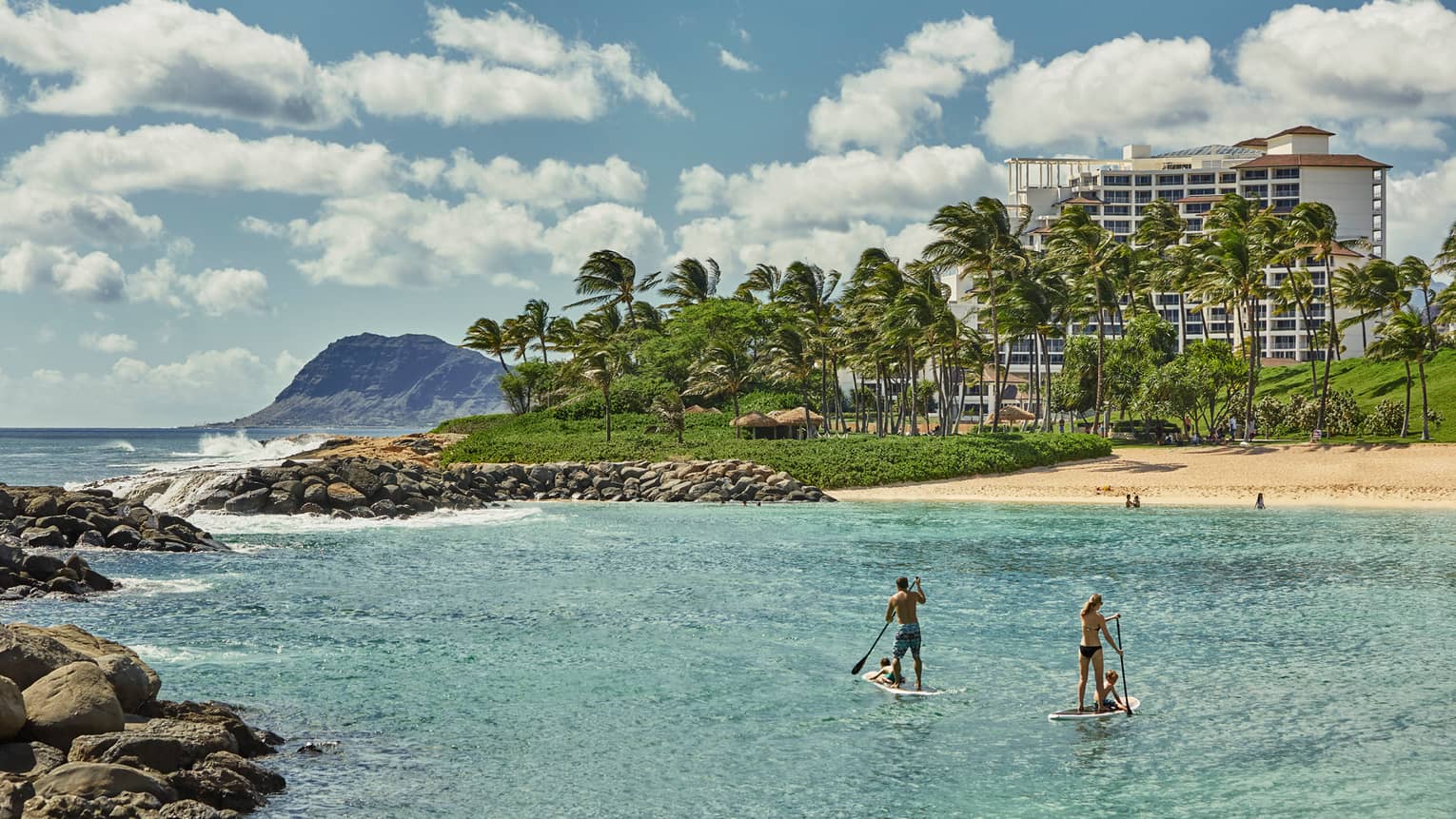 Two people on stand-up paddleboards in lagoon with beach and resort in background