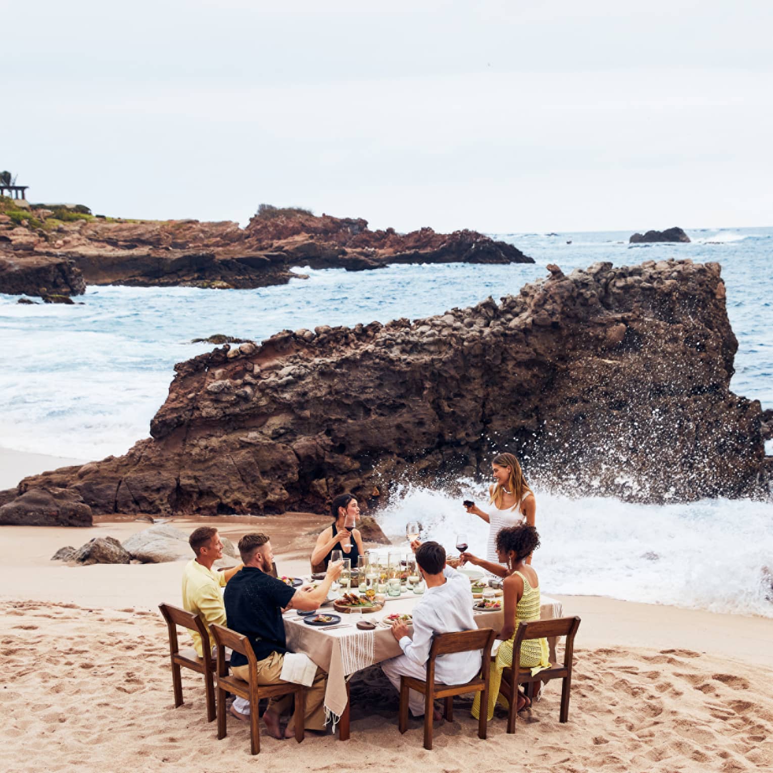 A group eating at a table on a beach with waves crashing nearby.