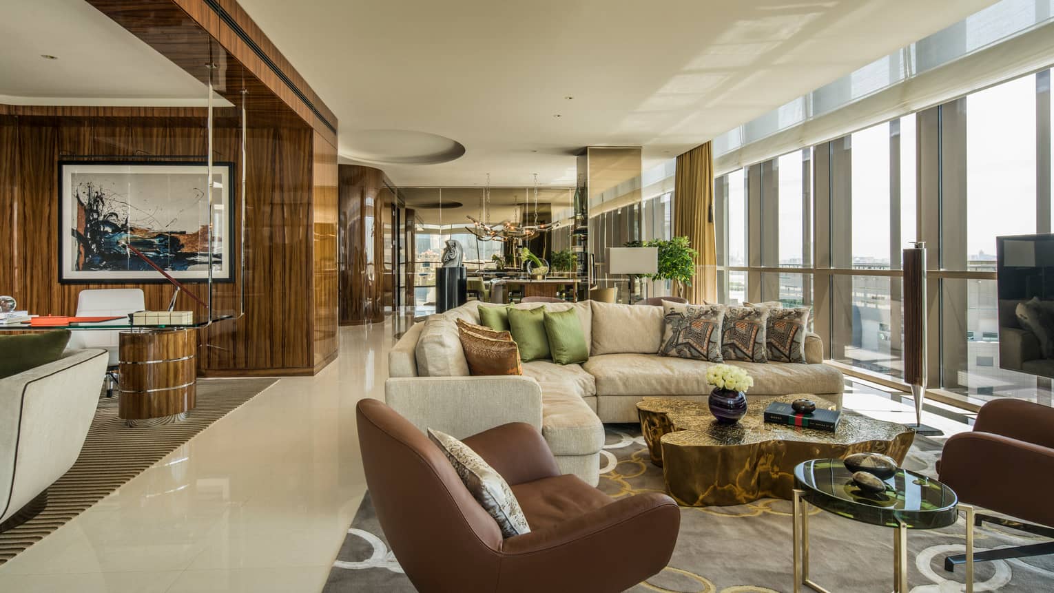 Penthouse Suite with large L-shaped beige sofa with pillows, leather armchairs, floor-to-ceiling windows along wall