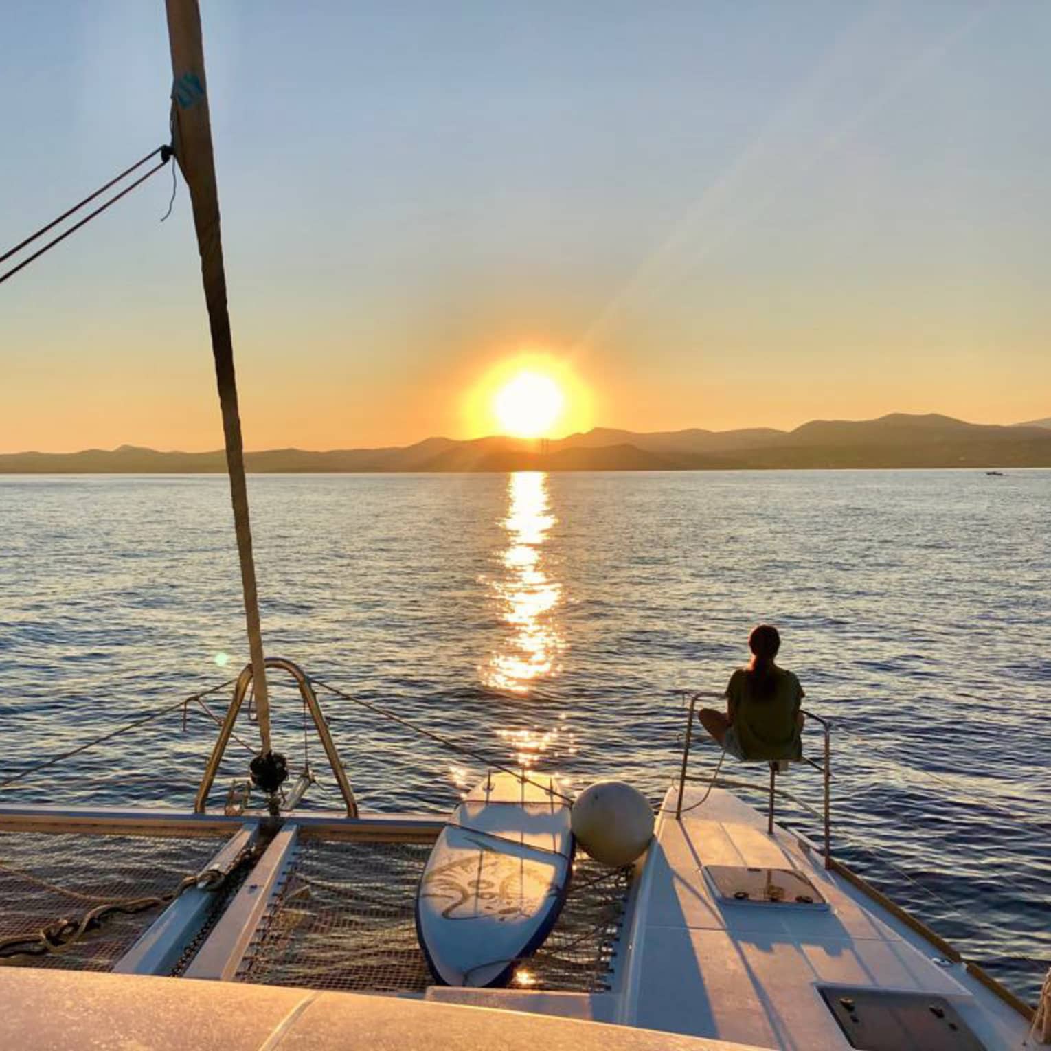 Two guests lounge on luxury sailboat near stern railing at sunset