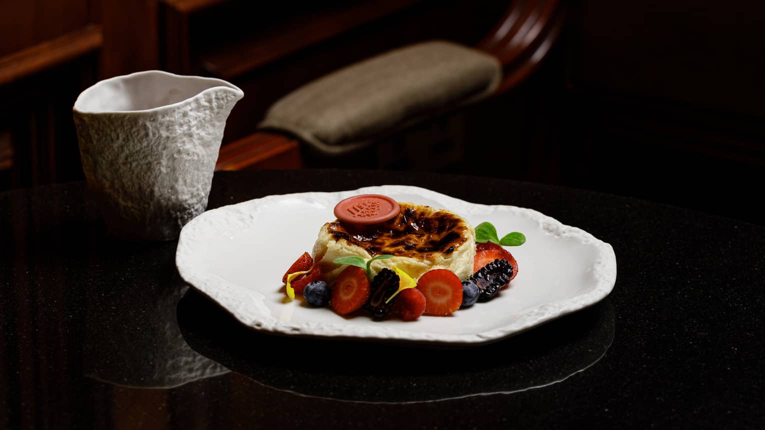 Cheesecake surrounded by fresh fruit slices served on a white dish on a dark table