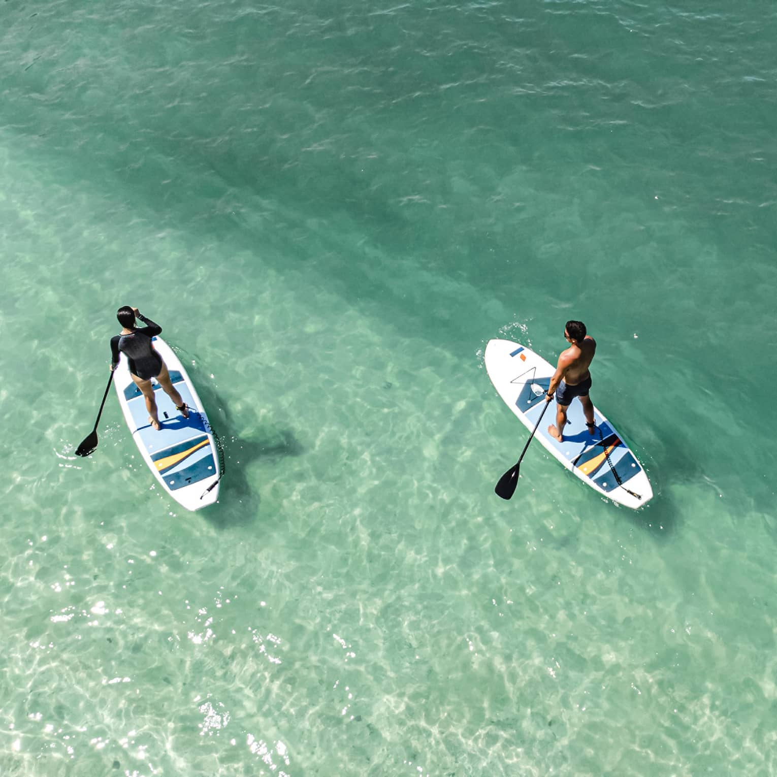 Aerial view of two people paddleboarding in clear green-blue water