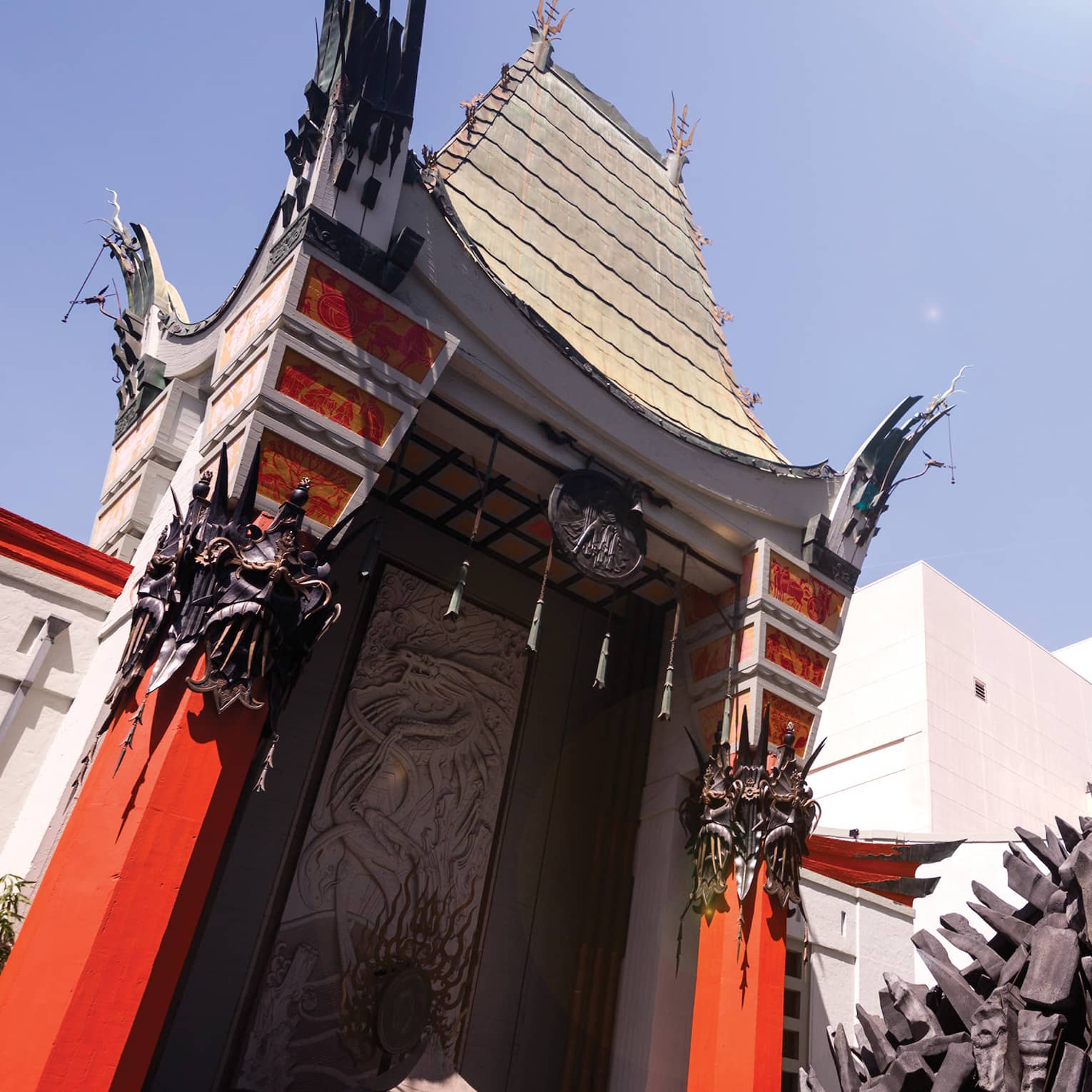 Towering into the sky, a curvy red and white building decorated with Chinese motifs stands behind a large statue of Godzilla.