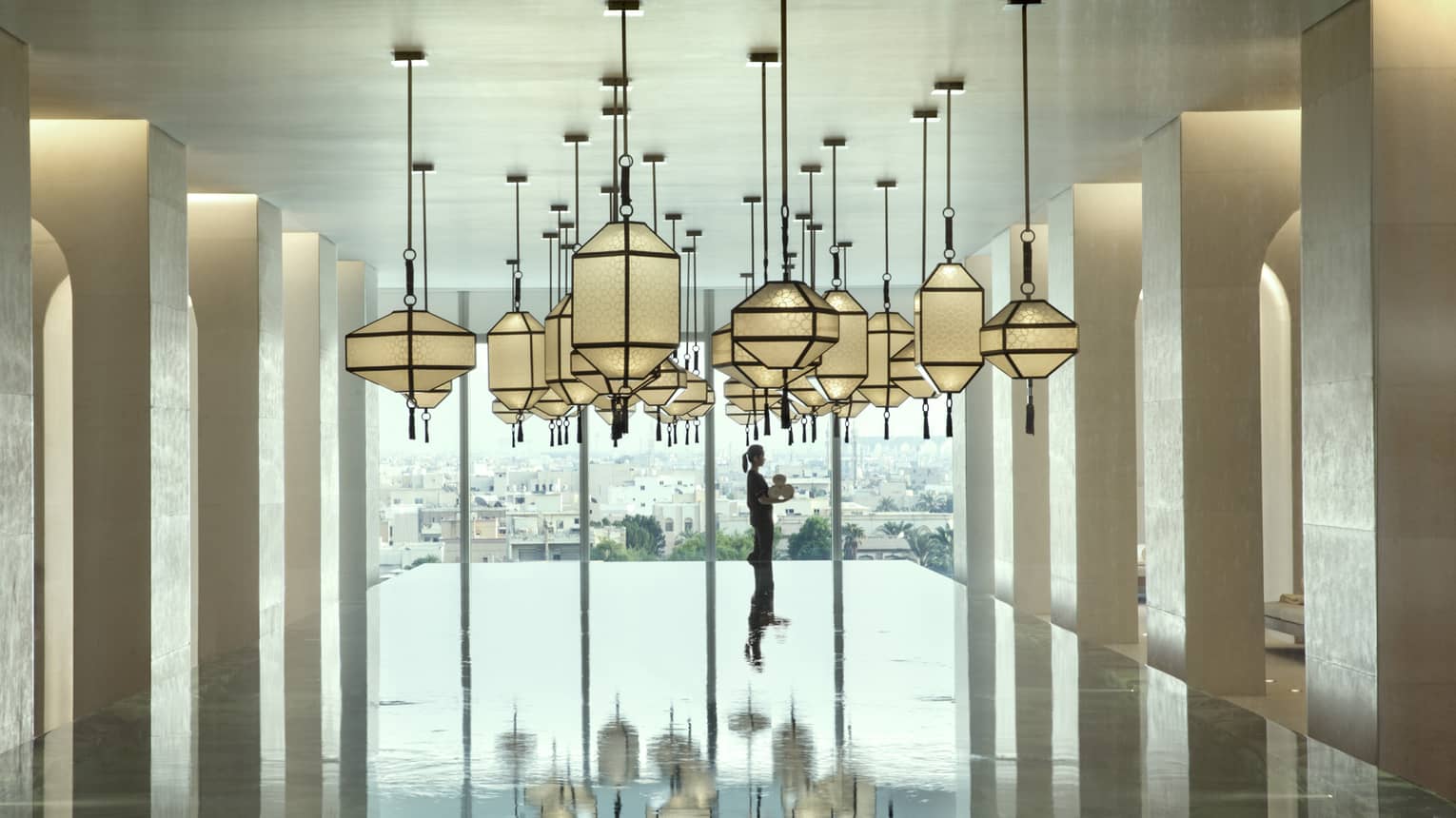 Hotel staff holds rolled white towels beyond large indoor swimming pool under dramatic lanterns