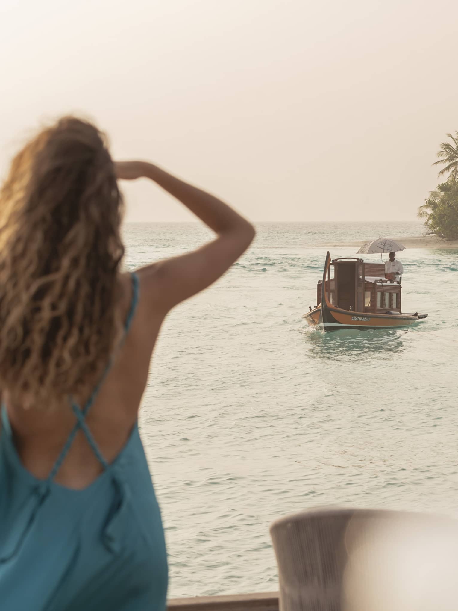 Person in blue dress shields eyes as boat travels toward shore