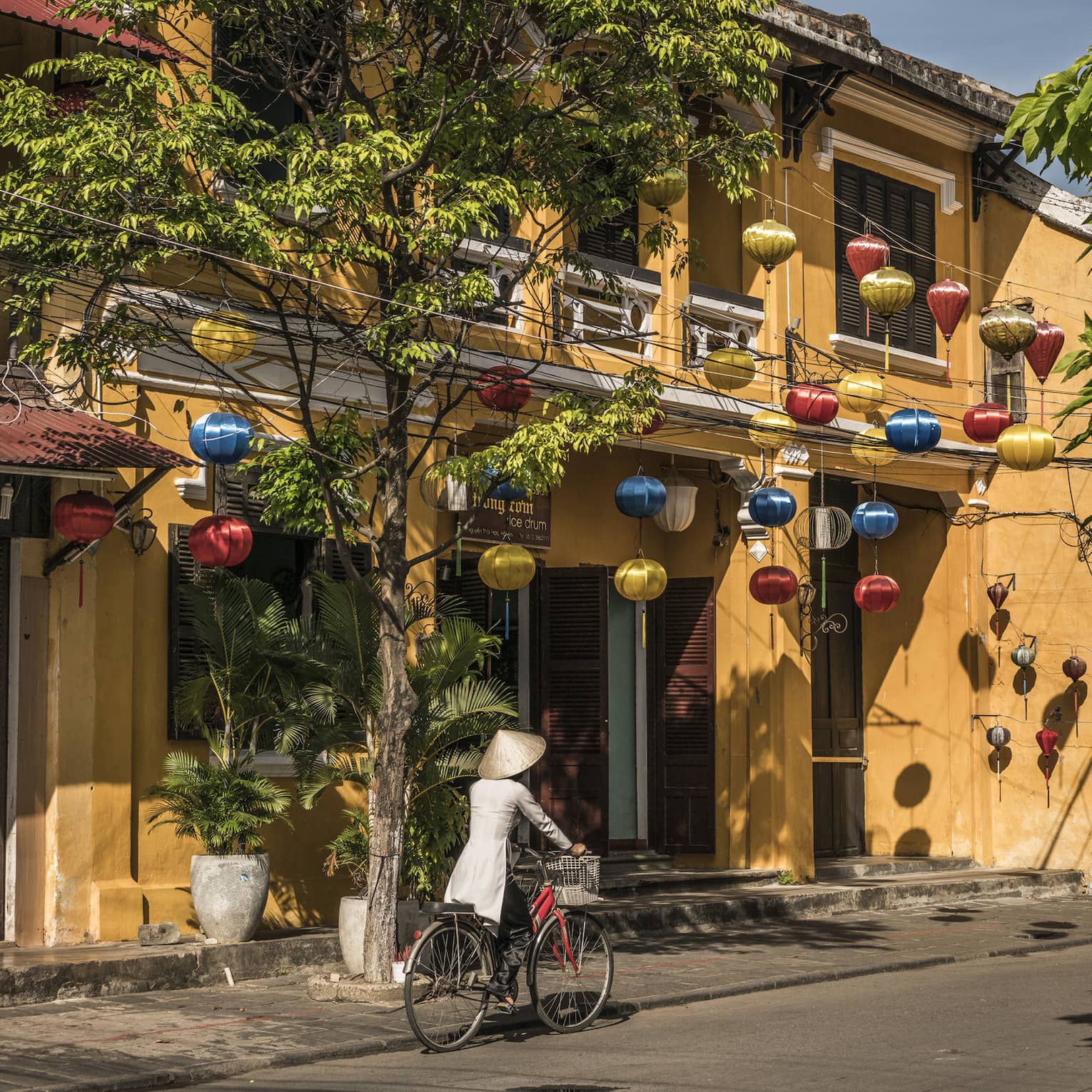 A woman biking down a historic street in Hoi, Viet Nam with lanterns along the side of a house 