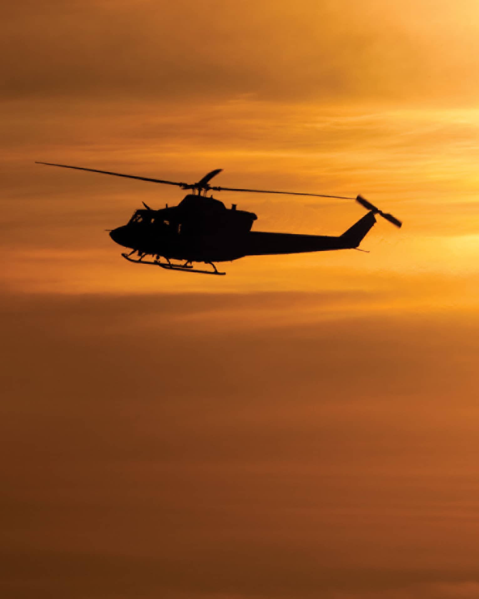 Silhouette of helicopter against orange sky