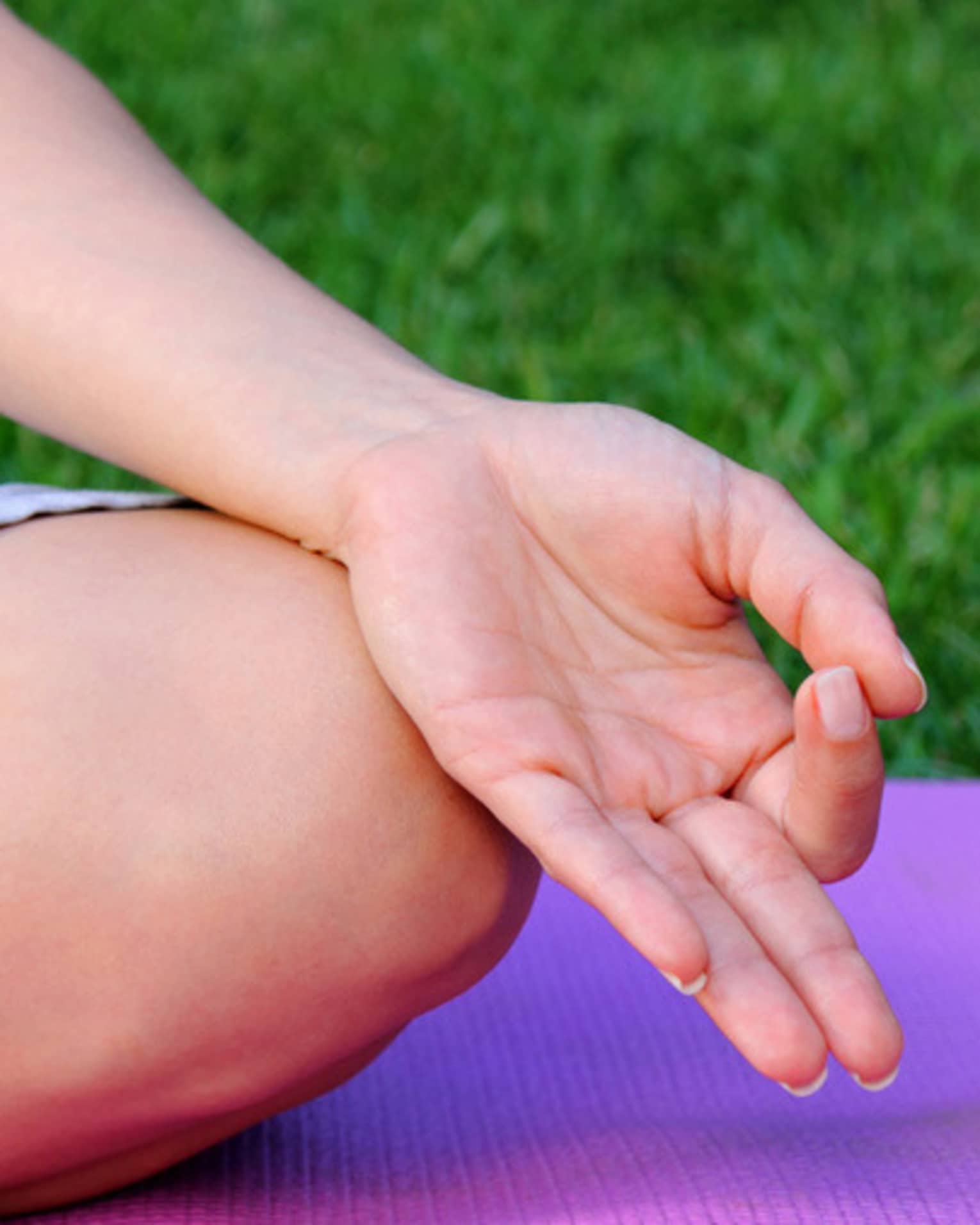 Side of hand, leg in cross legged meditation pose on yoga mat 