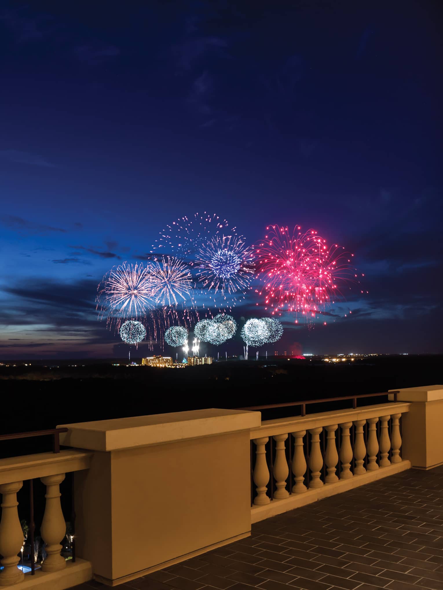 The terrace of a restaurant with tables and people watching fireworks in the distance.