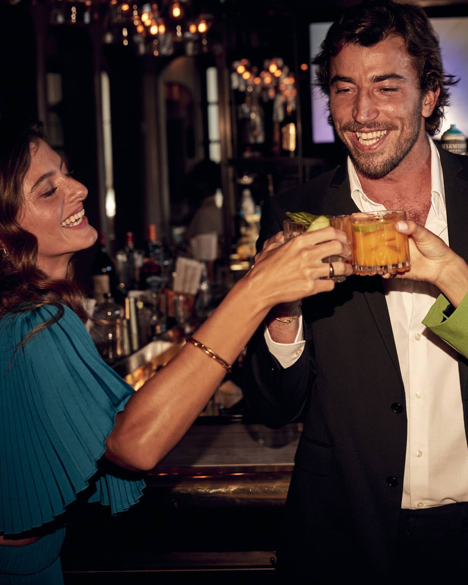 A man and two women toasting with drinks in hand at a bar.