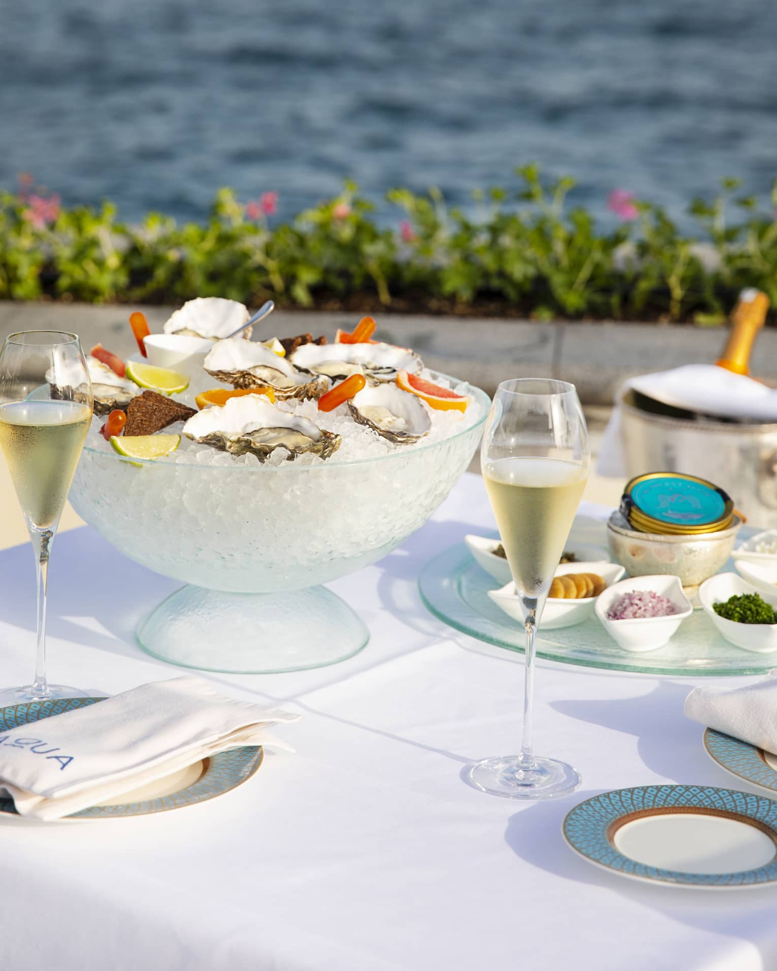Square table with white linens, blue dinnerware, a bowl of ice with oysters on the half shell, Sea of Marmara in the background