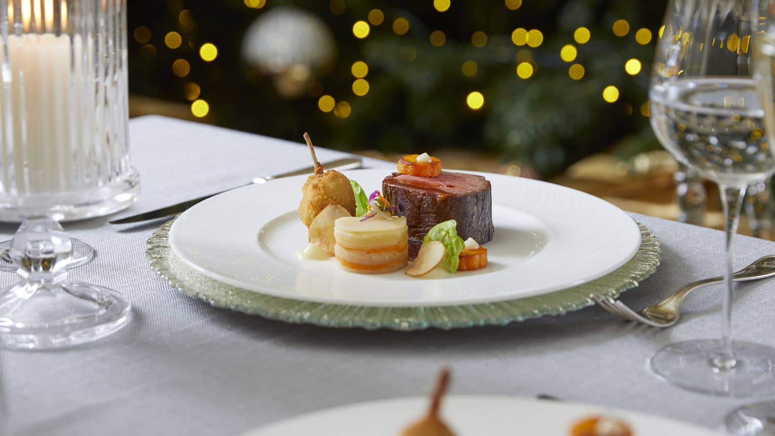 Dining table with a plate of food and wine glasses, and lights in the background.