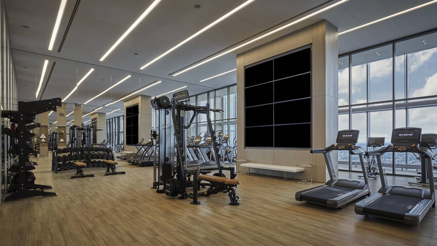 A spacious fitness center with large windows overlooking a city skyline