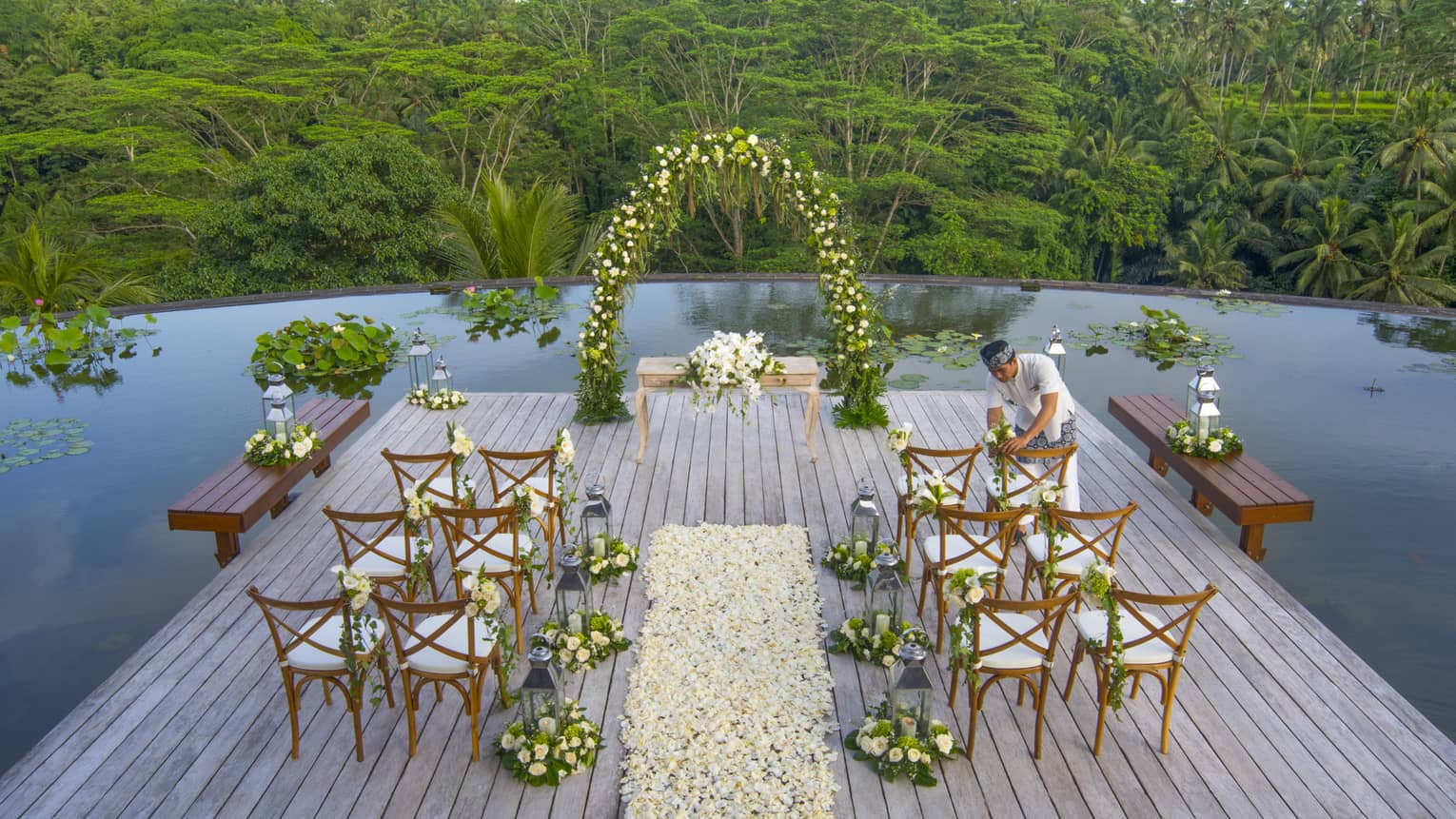 Staff sets flowers on chairs at small wedding reception on sunny platform over lily pond