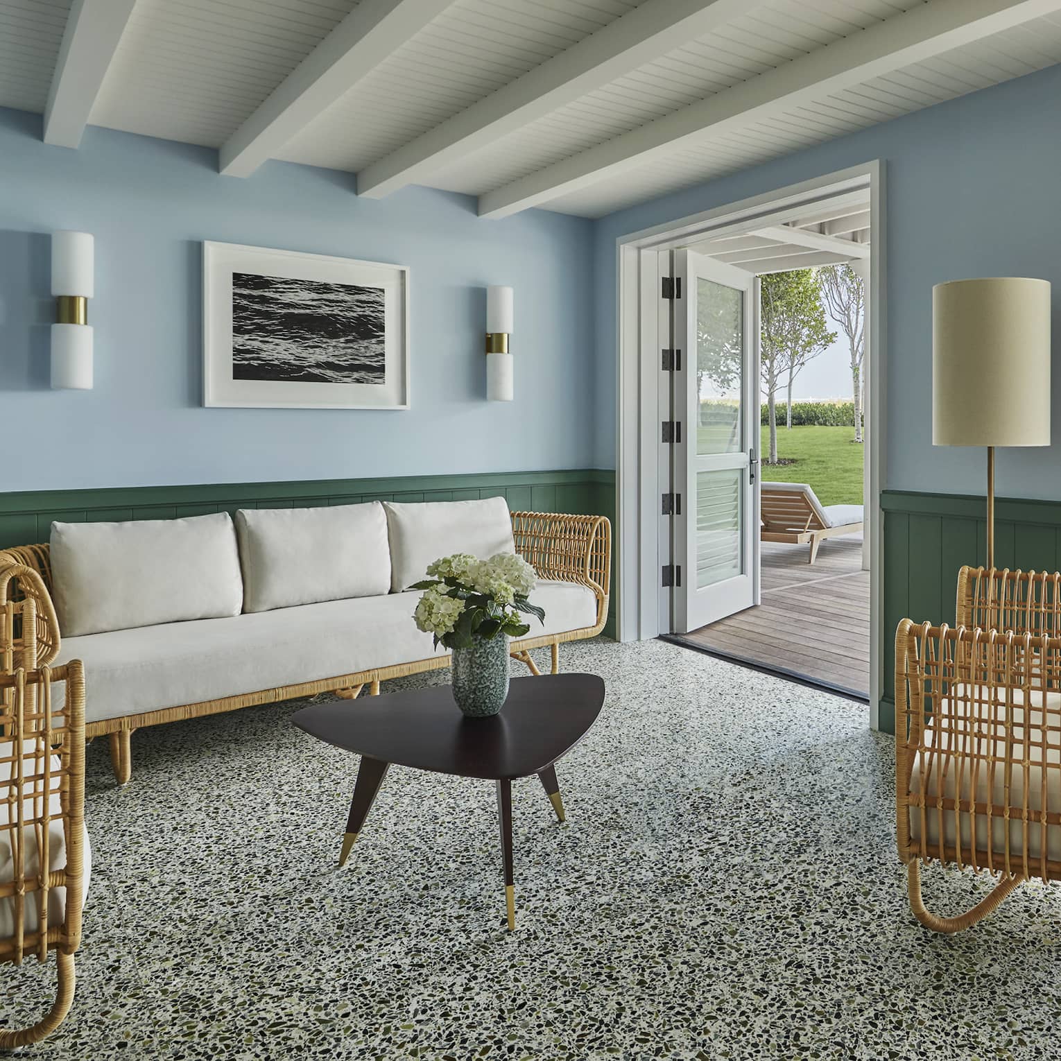 White-cushioned rattan furniture in a spacious living room of a private cabana, with double doors opening onto a scenic deck.