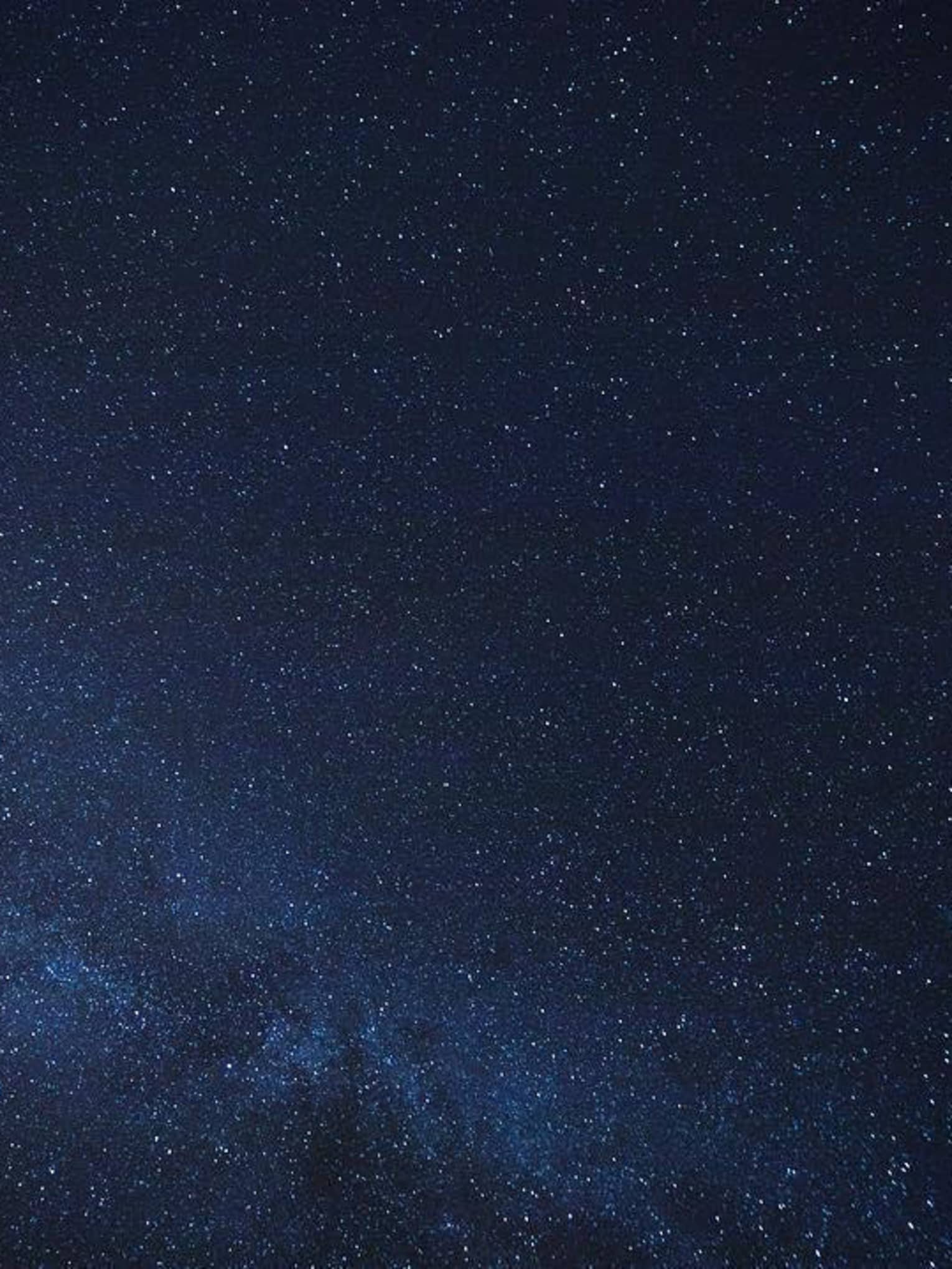 Thousands of stars dusting across a clear night sky; a cluster of stars form the Milky Way, just barely visible in the sky.